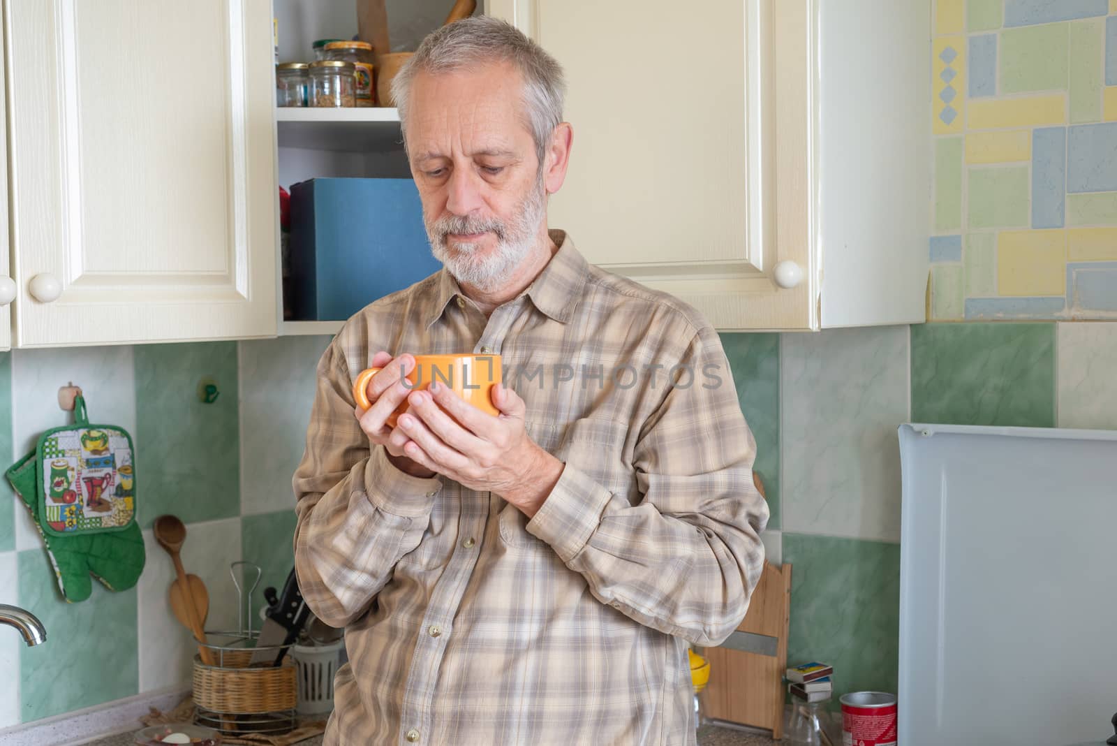 Mature man drinking his coffee in an orange cup, at morning in kitchen