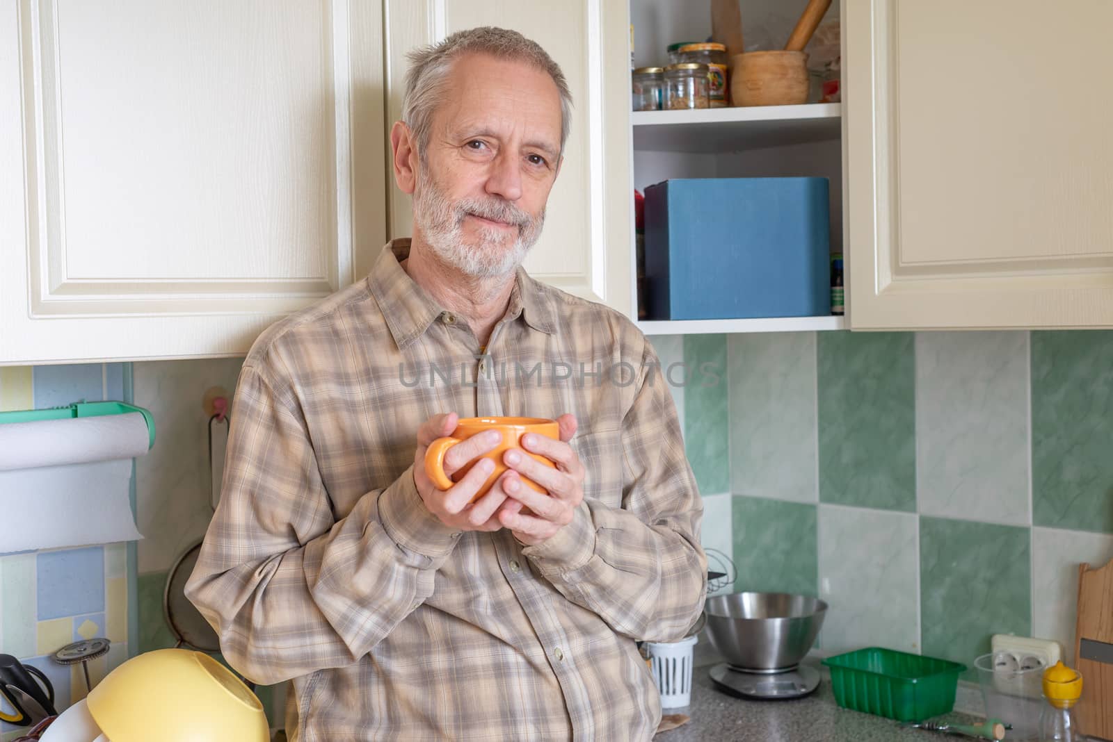 Mature man drinking his coffee in an orange cup, at morning in kitchen