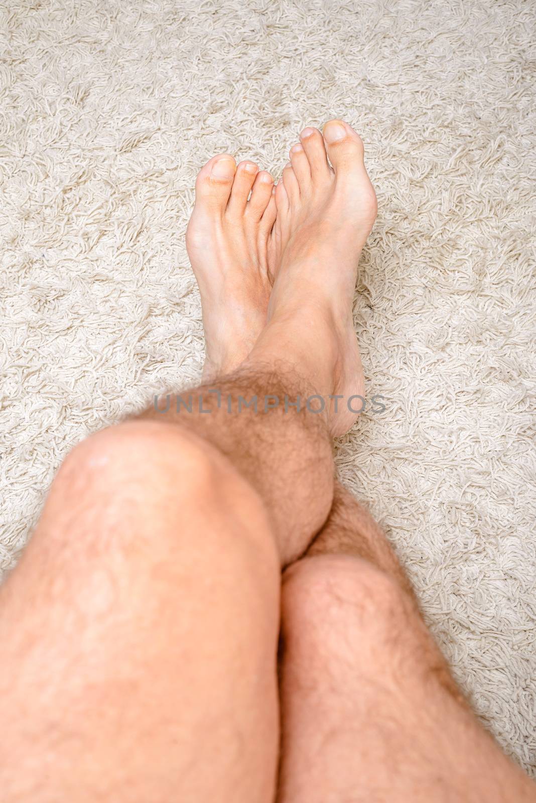 A man is relaxing, the feet on a warm wool carpet, and showing hairy legs