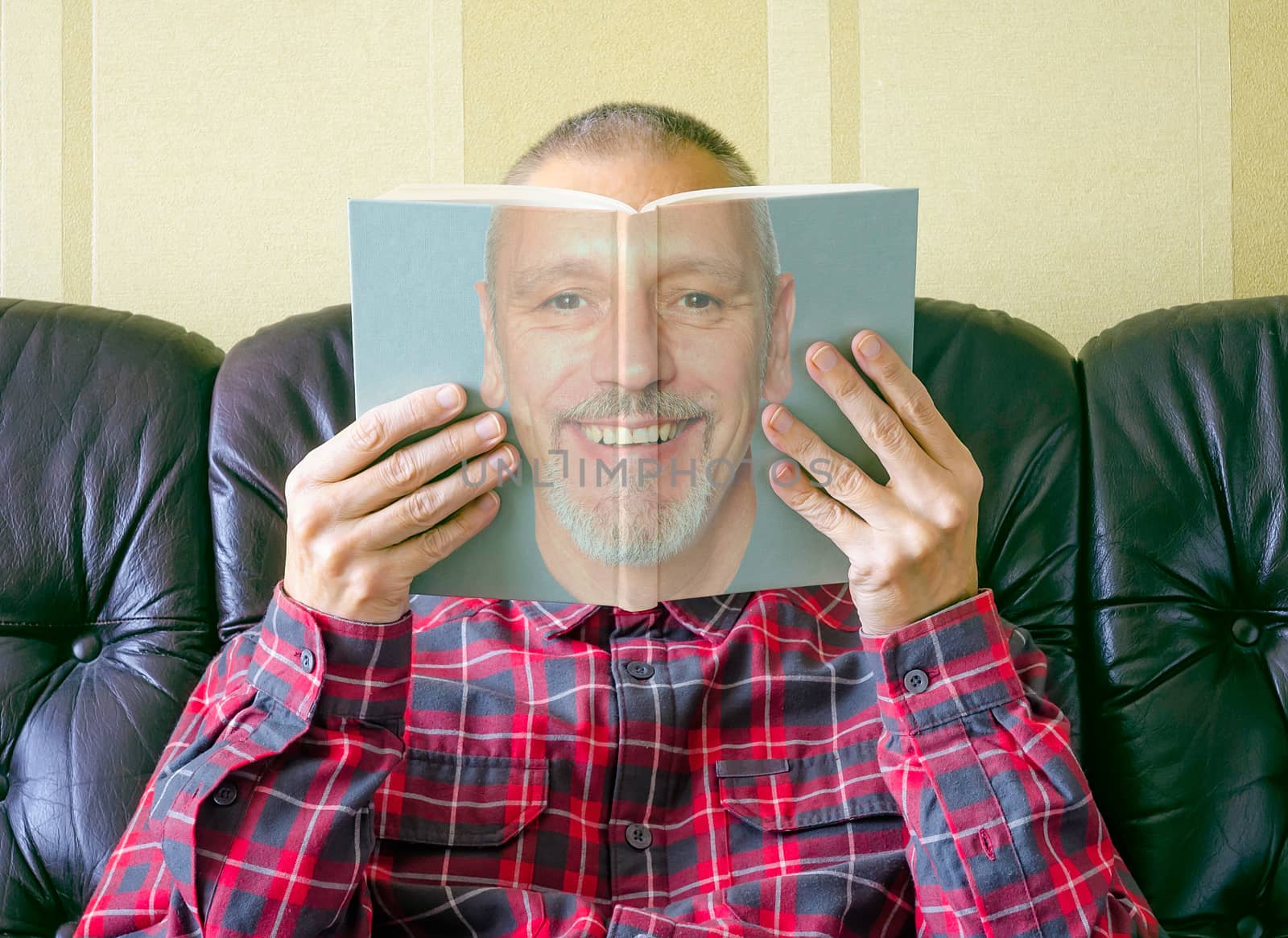 A man reading a book about himself, with his face seen on the cover.