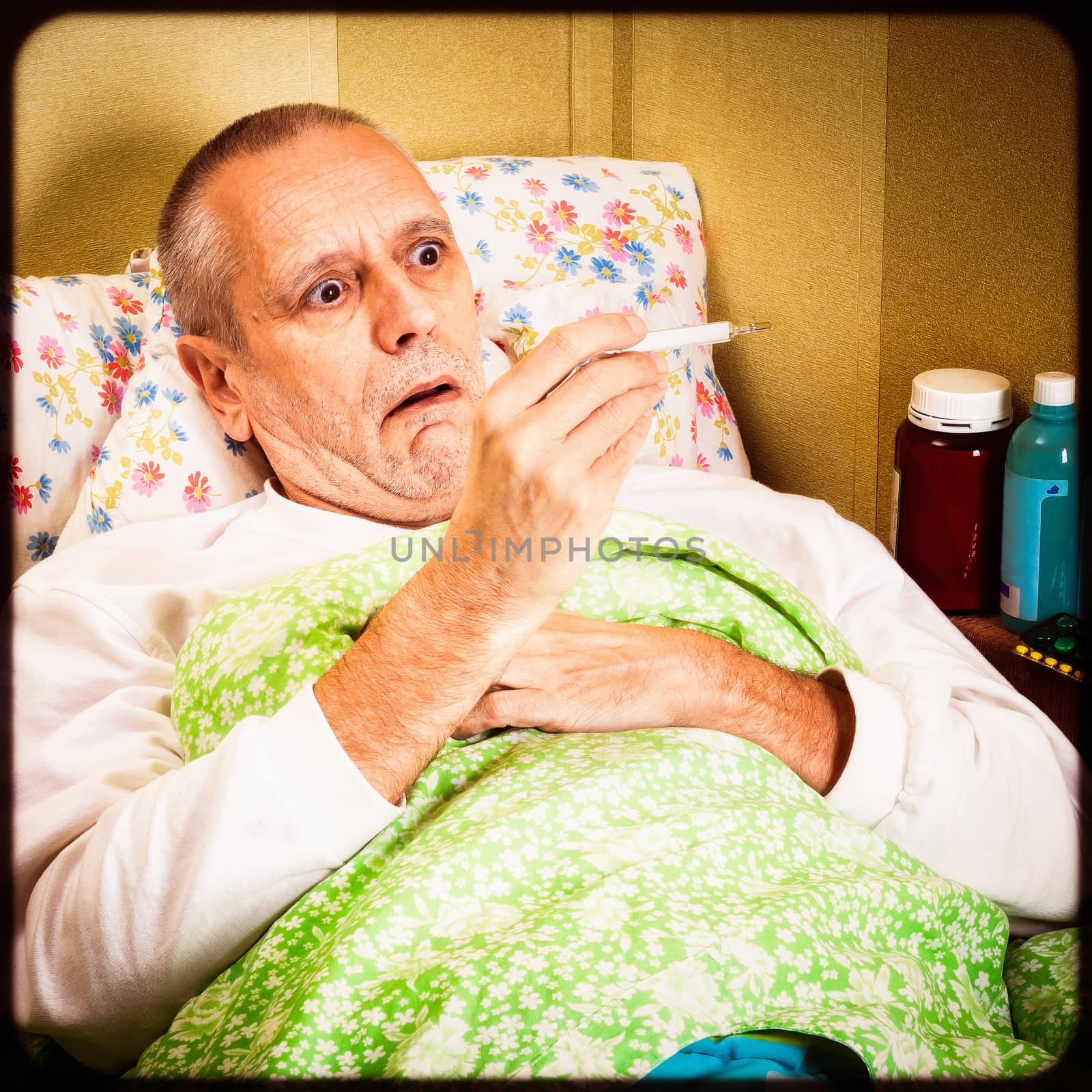 Sick man lying in bed and measuring the temperature with a thermometer