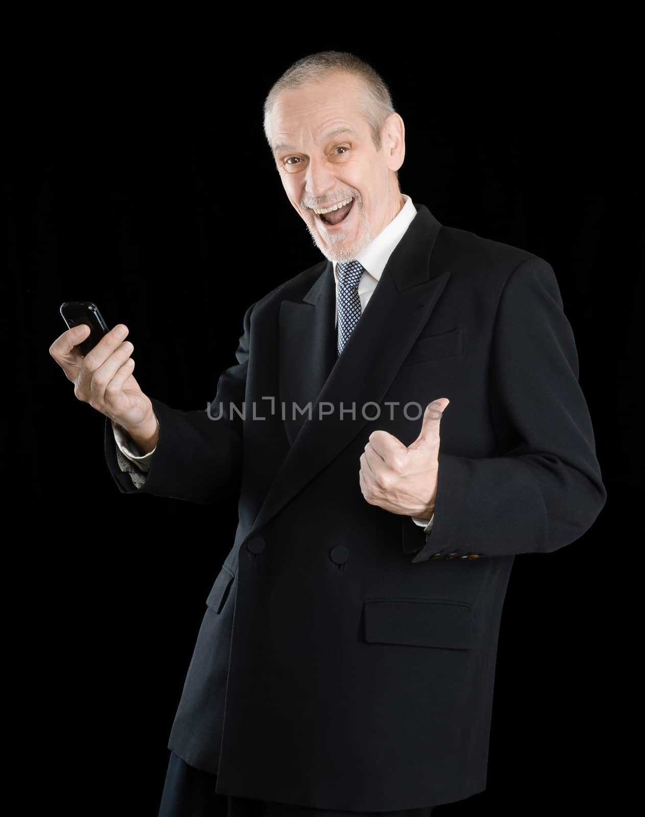 Happy businessman wearing a black suit, smiling and reading sms on mobile phone, with thumb up, on black background