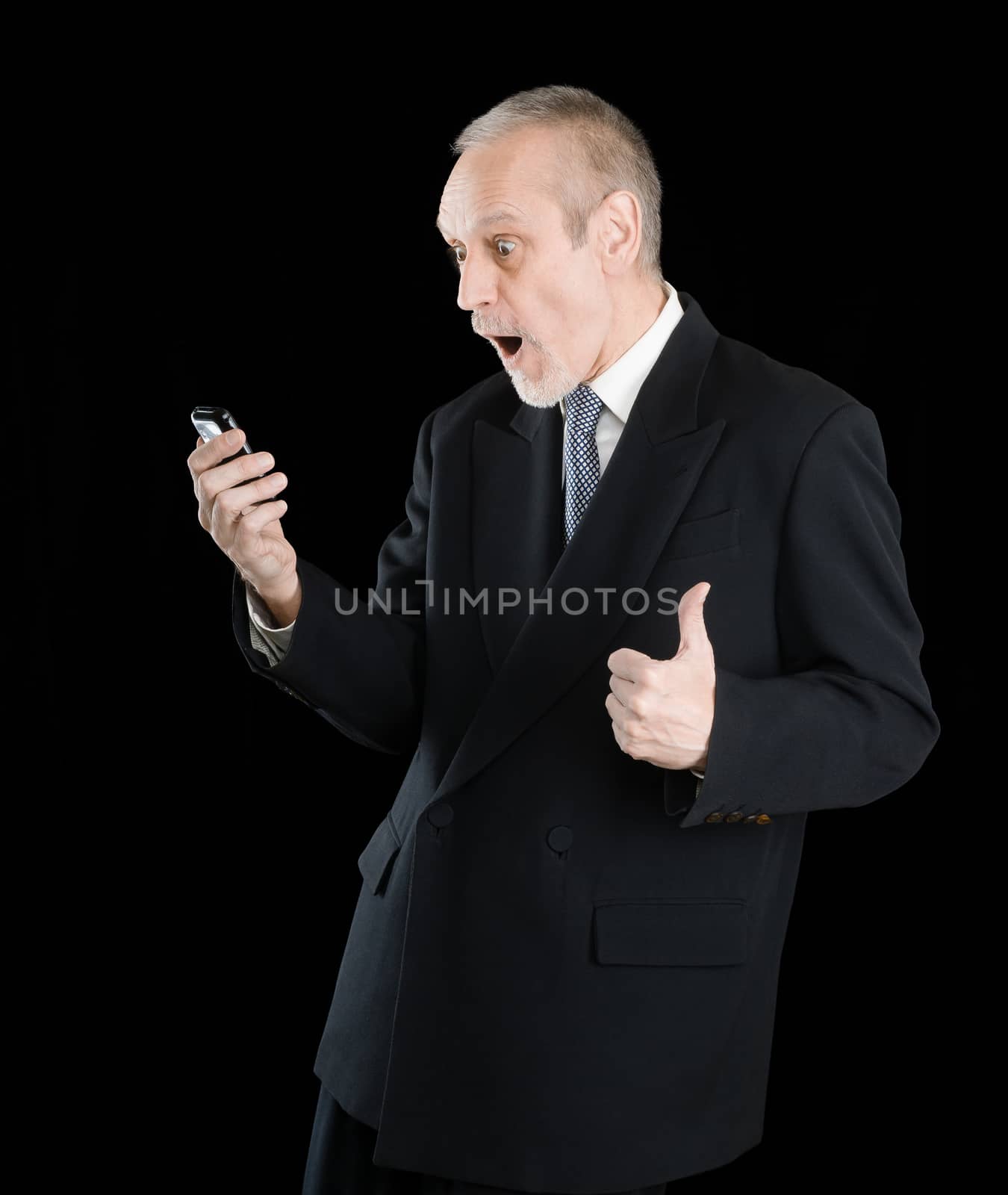 Happy businessman wearing a black suit, smiling and reading sms on mobile phone, with thumb up, on black background