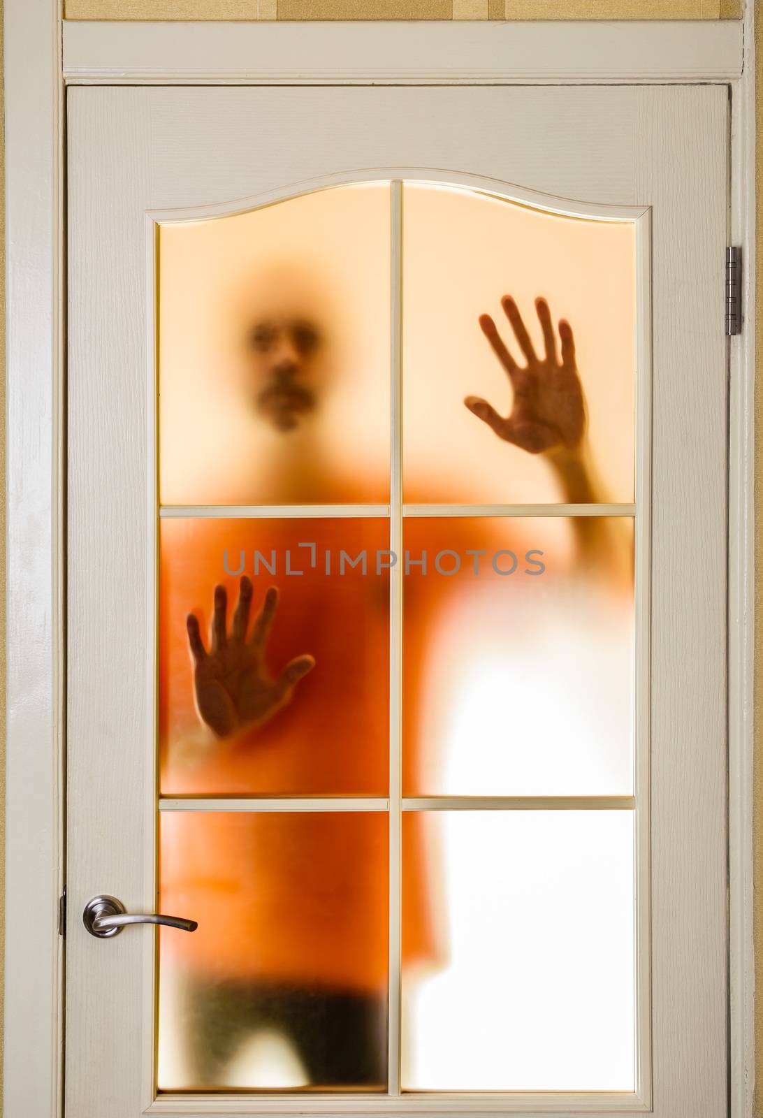 Silhouette of an unknown man in orange seen behind a closed glass door, like a ghost or an alien