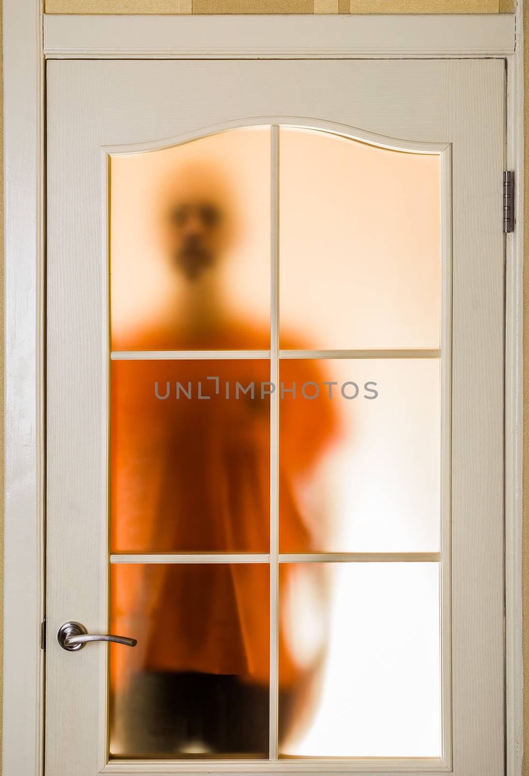 Silhouette of an unknown man in orange seen through a closed glass door, like a ghost or an alien