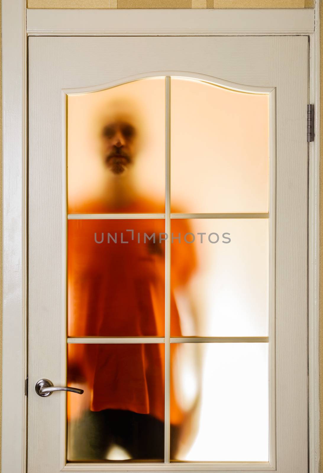 Silhouette of an unknown man in orange seen through a closed glass door, like a ghost or an alien