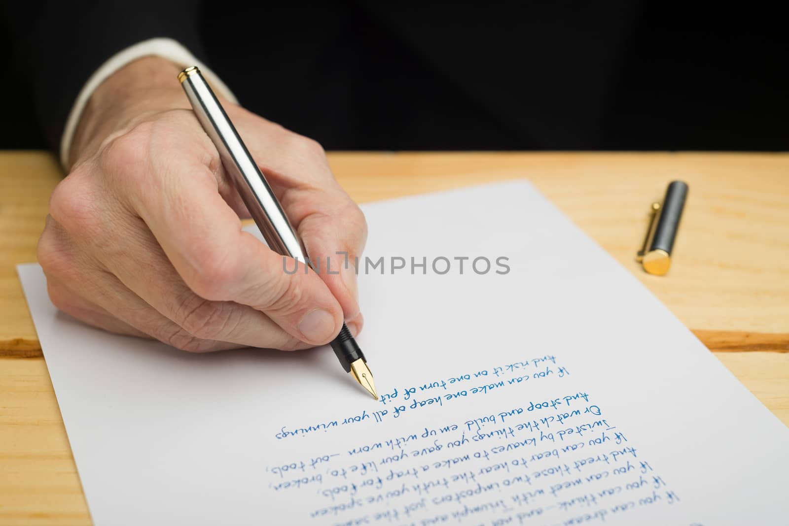 A businessman writing with a fountain pen on a white paper set on a wooded deck