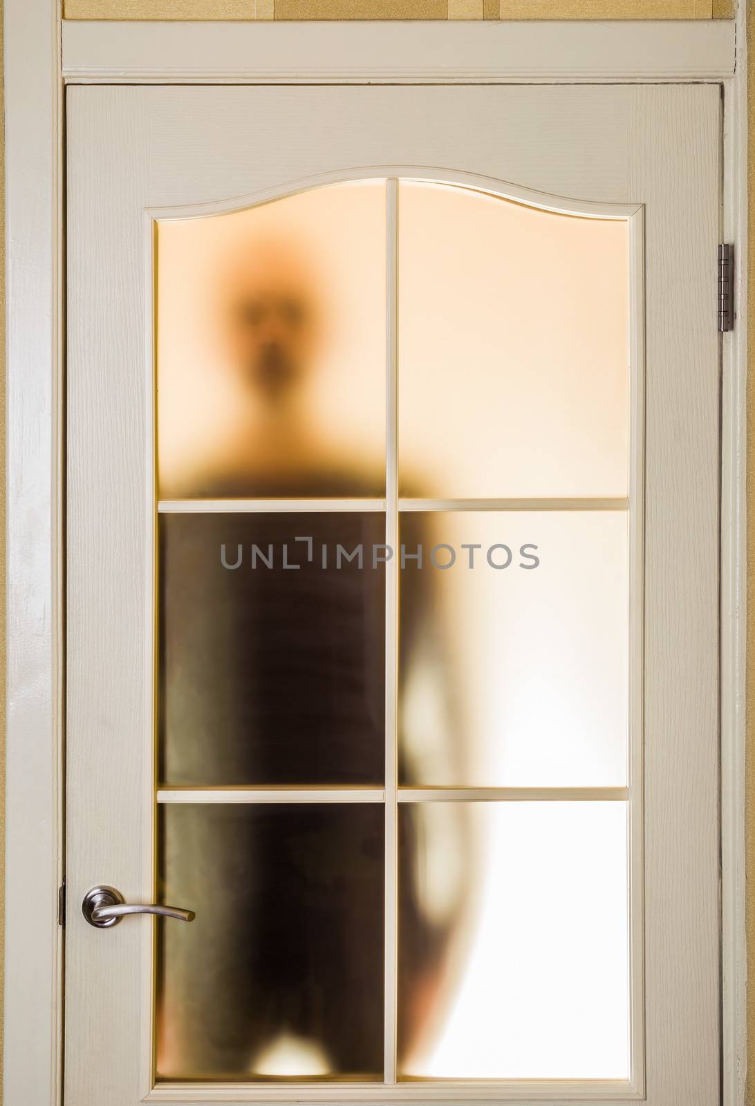 Silhouette of an unknown man in black seen through a closed glass door, like a ghost or an alien