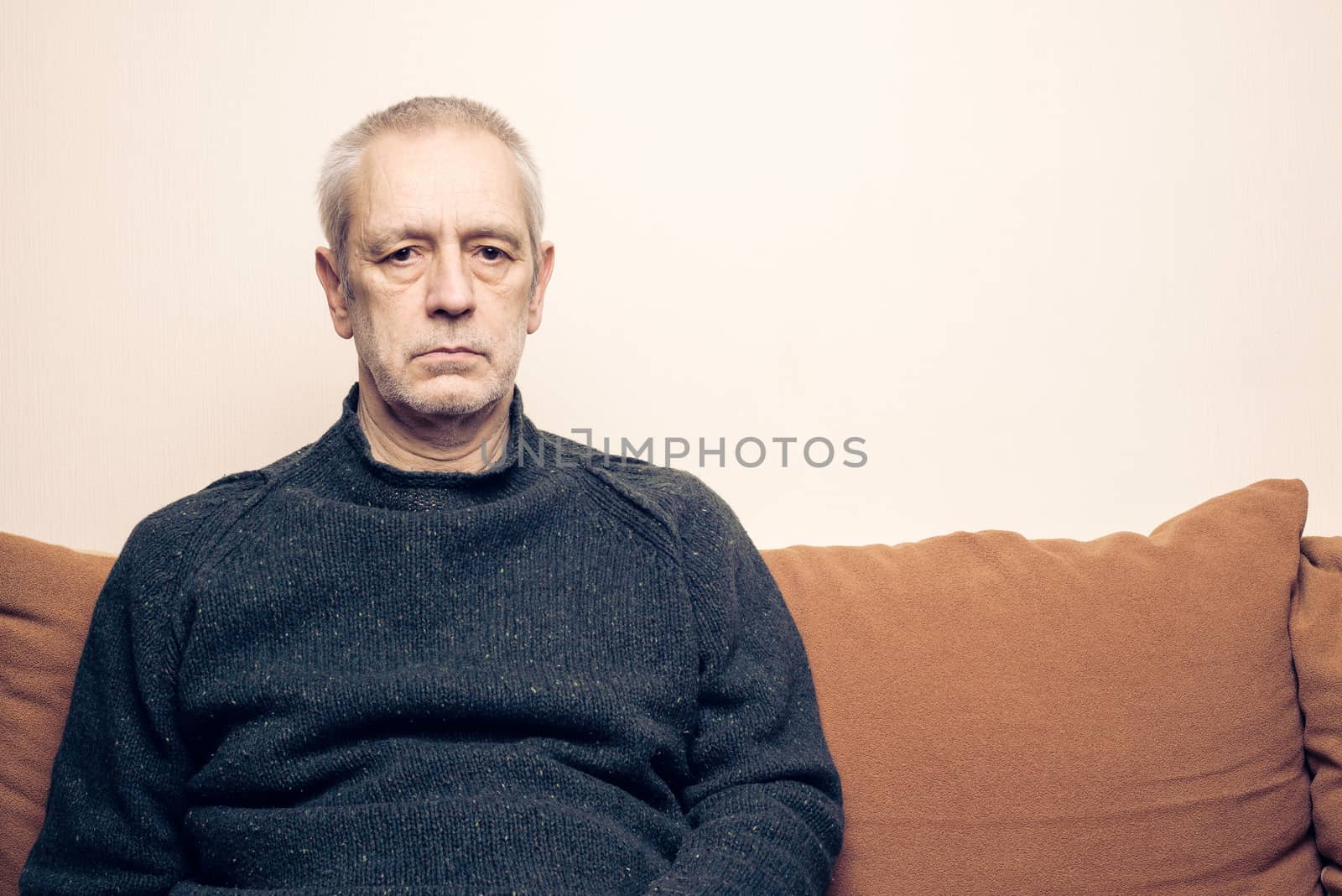 Dramatic portrait of a sad and depressed adult man sit on a sofa and  looking into space with lackluster eyes. Negative space for copy text