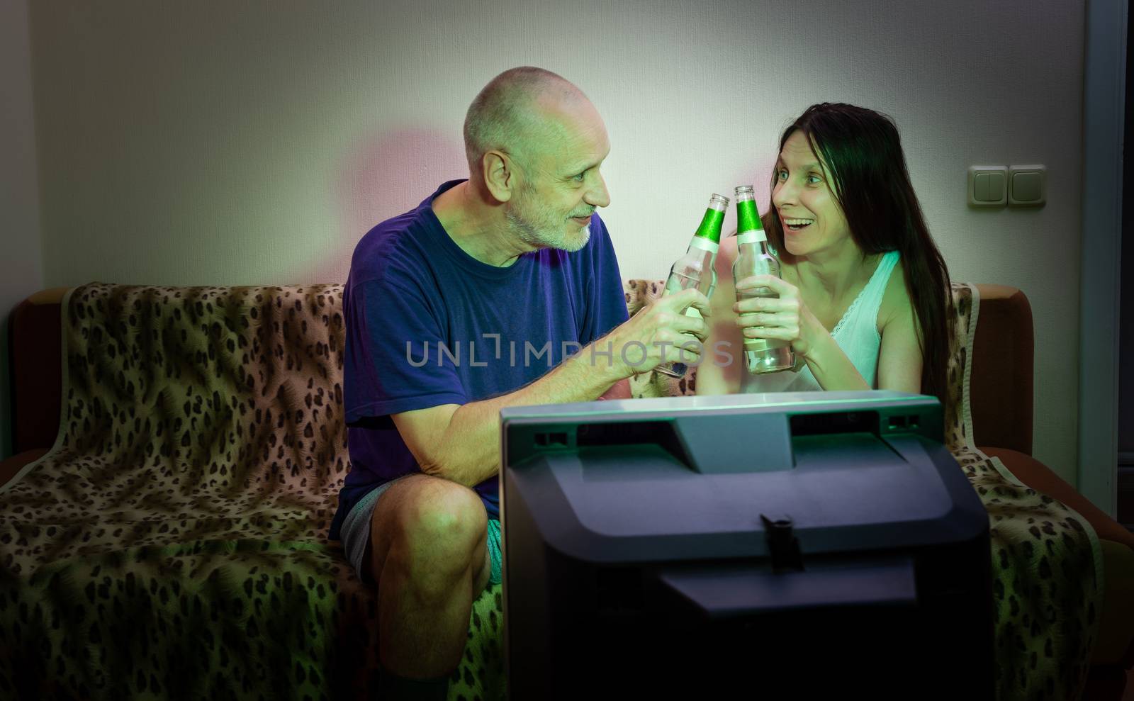 An adult man and woman watch sports on television in their small by MaxalTamor