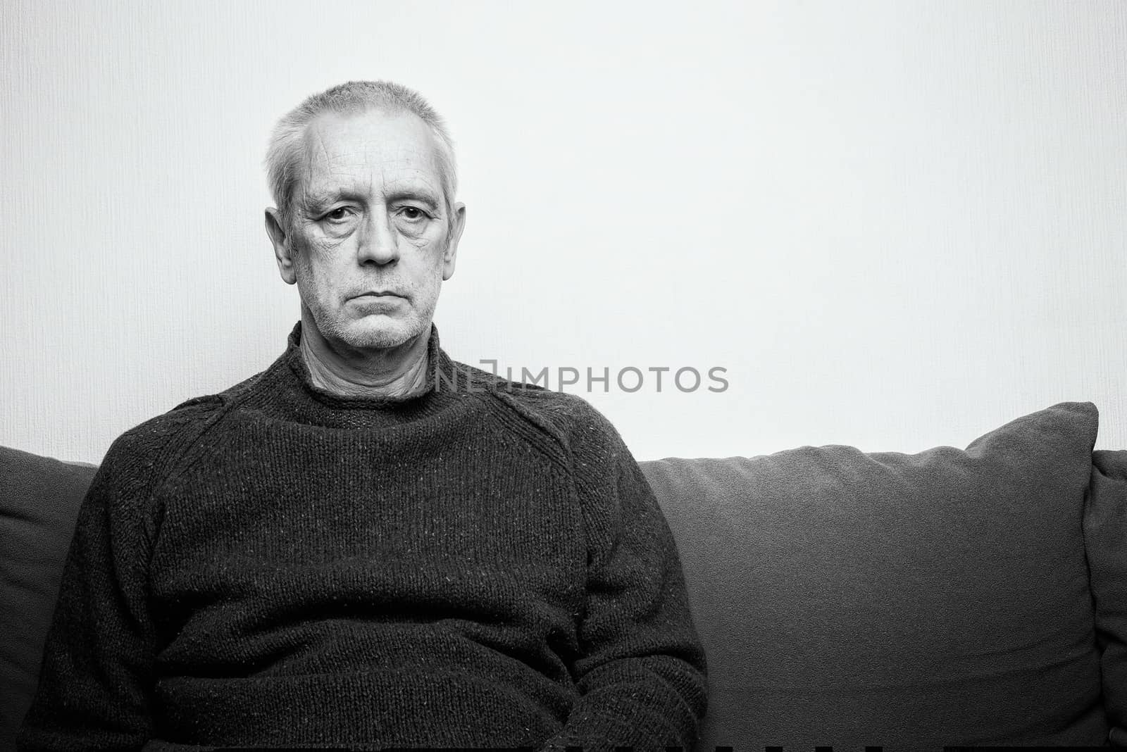 Dramatic portrait of a sad and depressed adult man sit on a sofa and  looking into space with lackluster eyes. Negative space for copy text