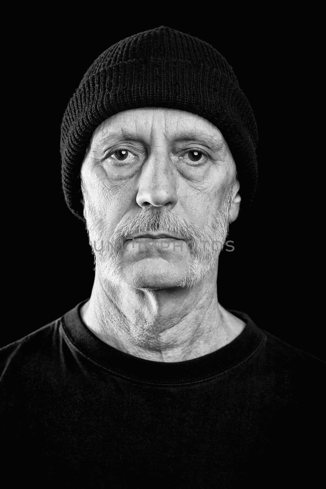 Dramatic black and white portrait of a serious and confident caucasian man with a penetrating gaze and a bit of neutral expression in the eyes, wearing a woolen cap on the head