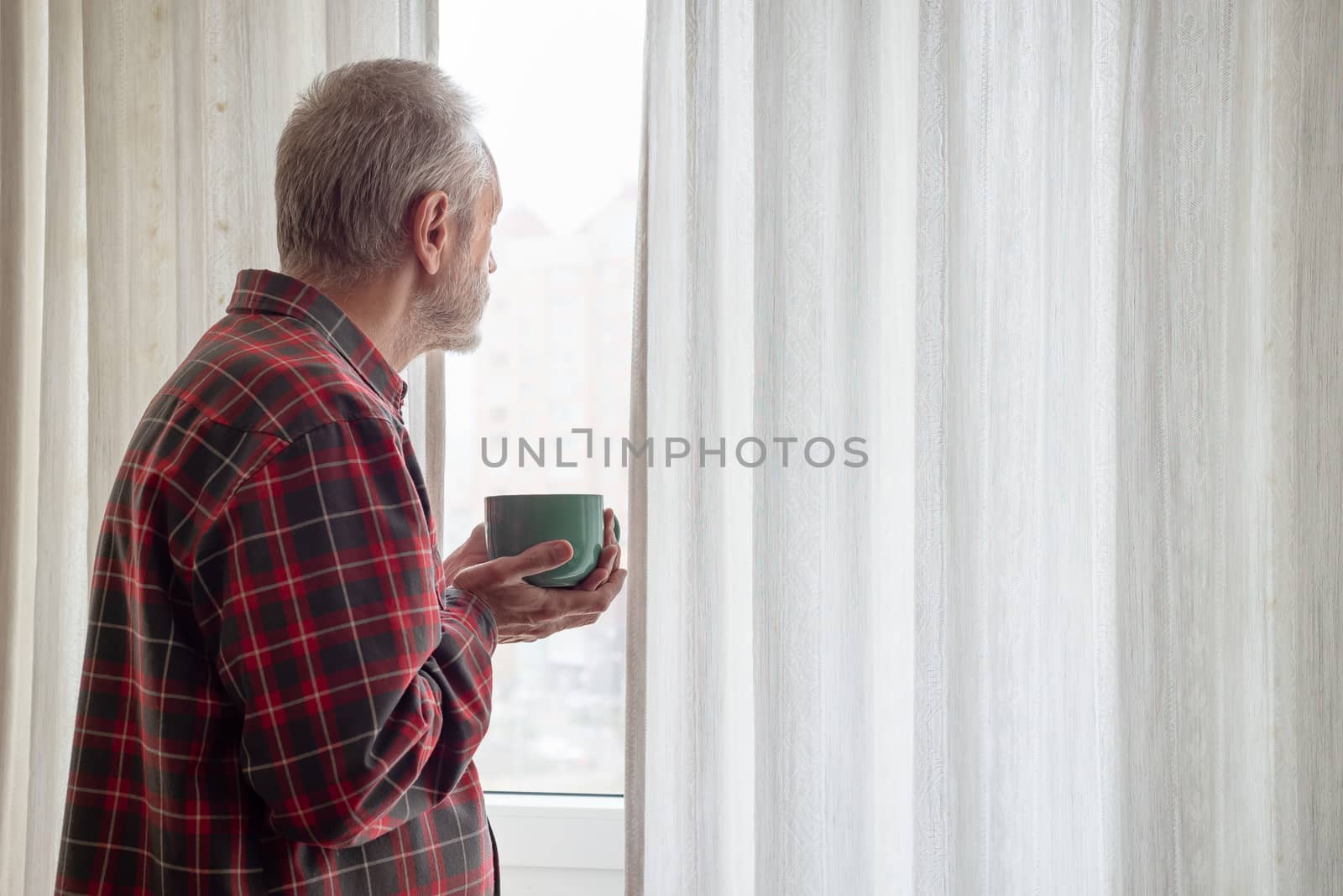 Mature man drinking his coffee in a green cup, while he is looking out of the window