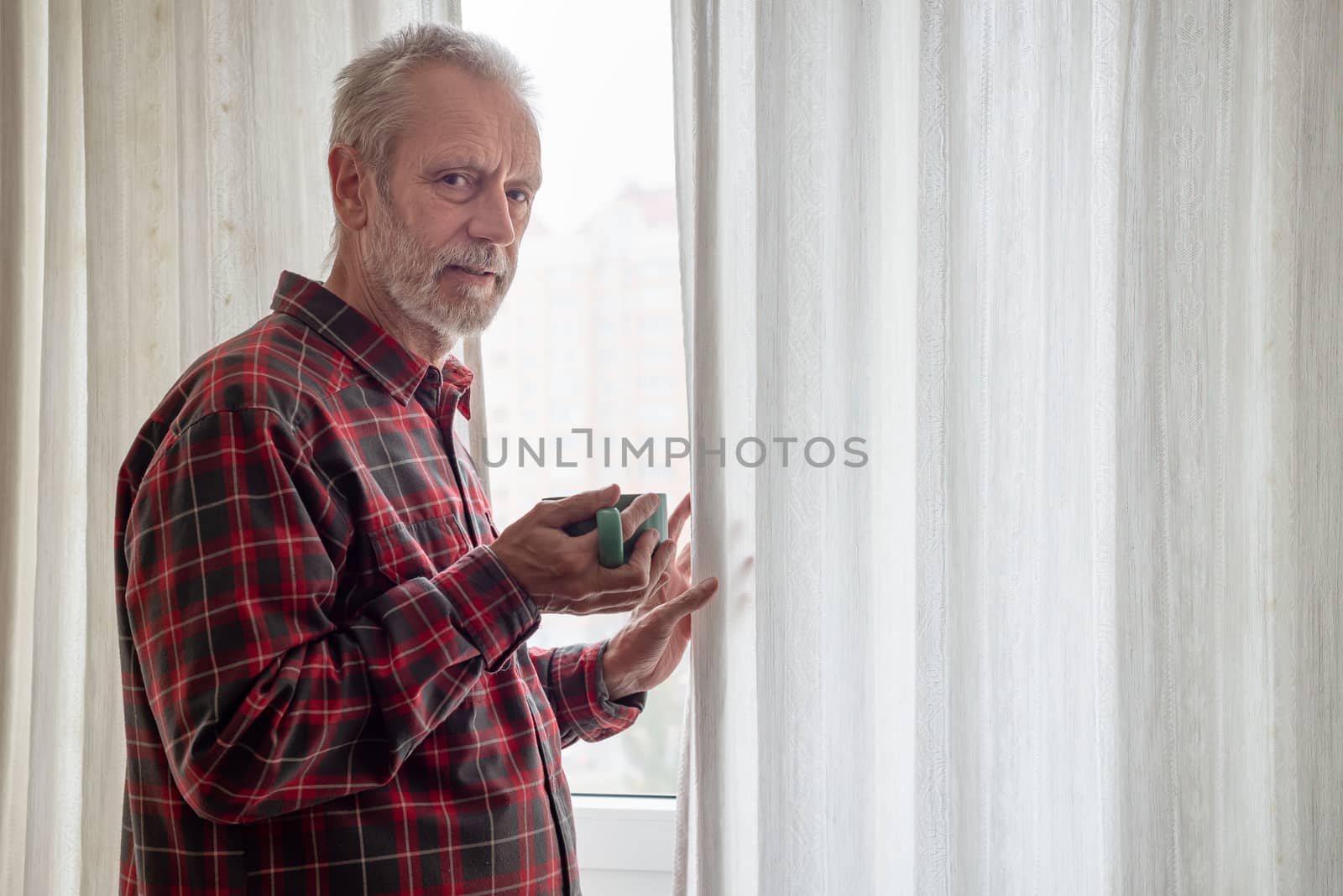 Mature man drinking his coffee in a green cup, while he is looking out of the window