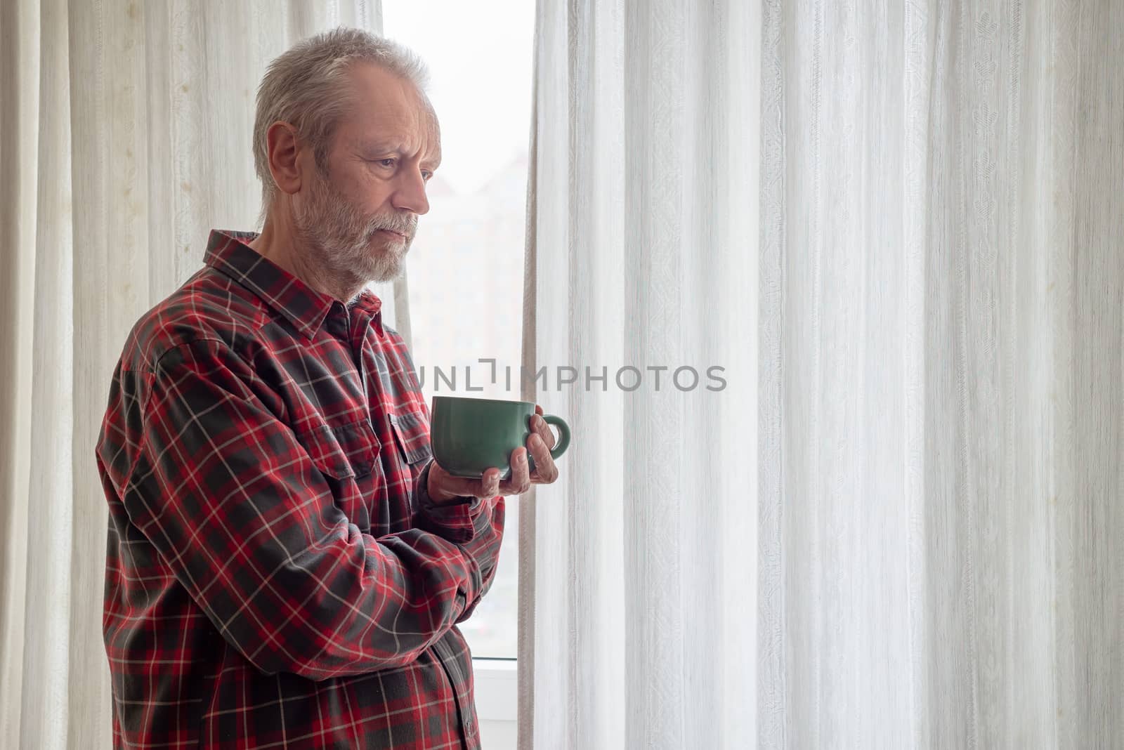 Sad mature man drinking his coffee in a green cup, while he is looking out of the window