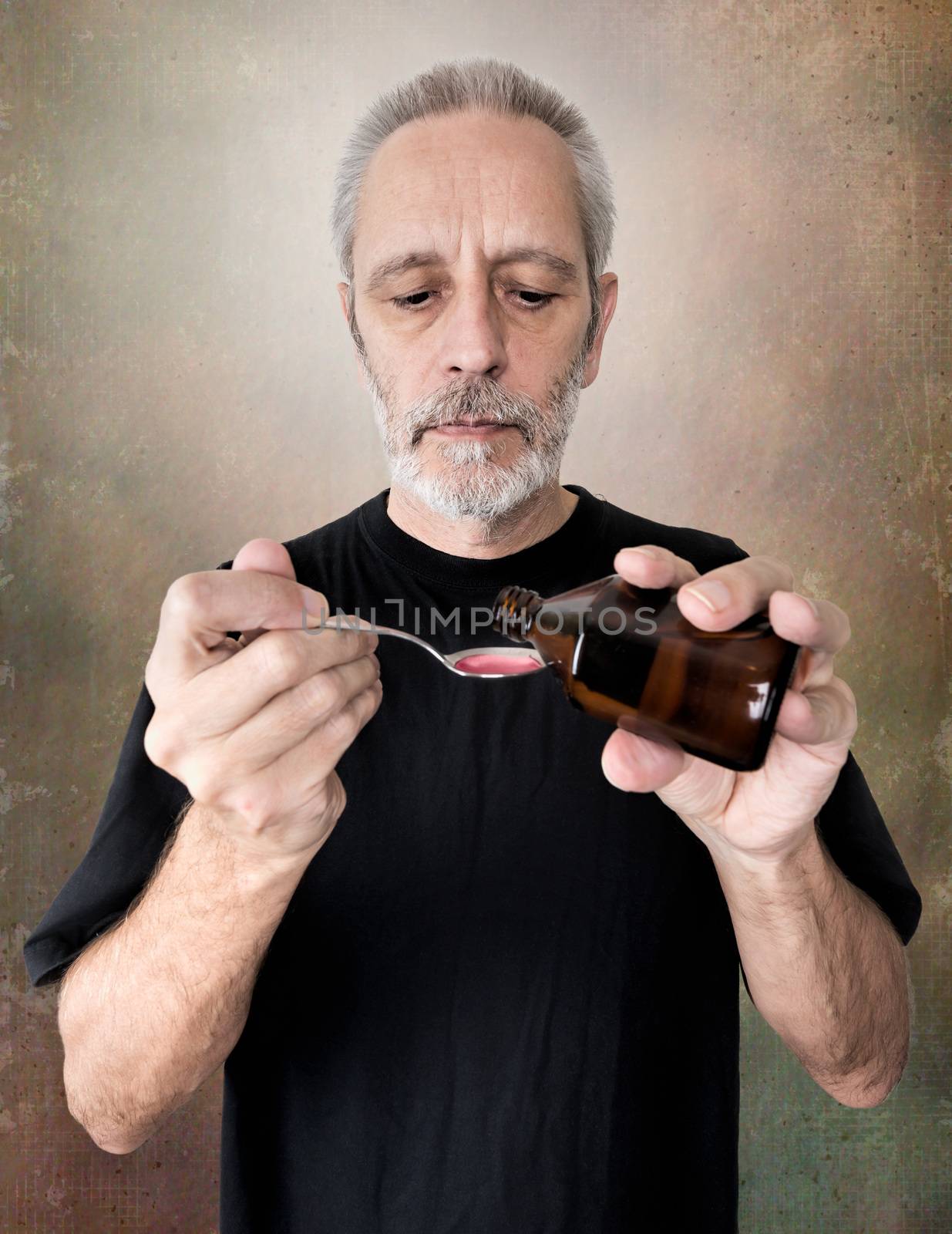 A mature man is pouring cough syrup in a spoon to cure his sore throat and bronchitis