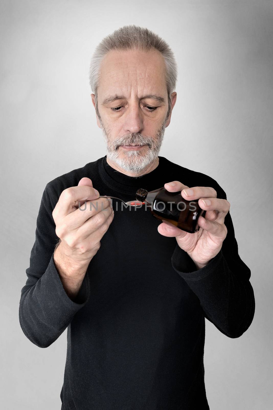 A mature man is pouring cough syrup in a spoon to cure his sore throat and bronchitis