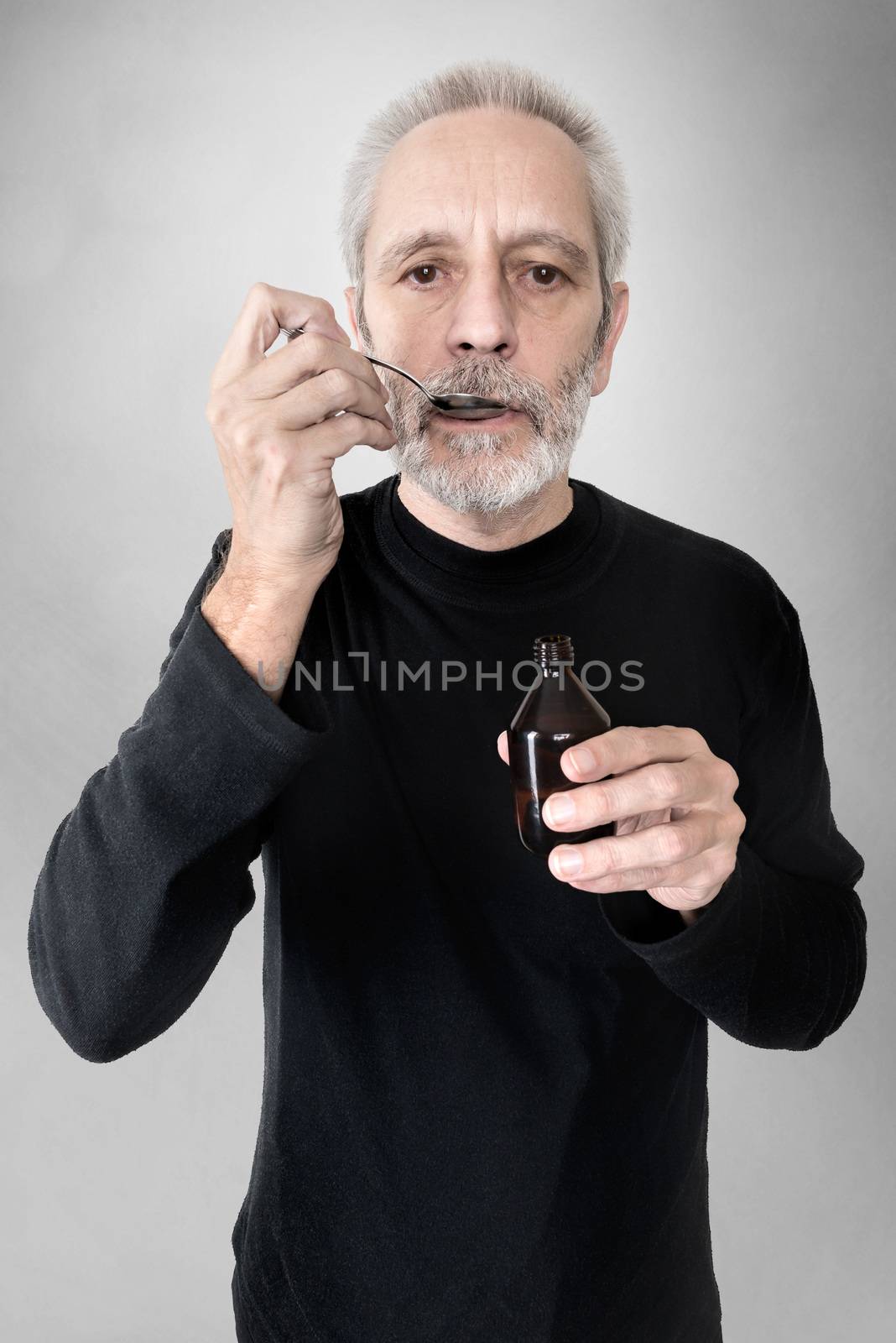 A mature man is drinking a spoon of  cough syrup to cure his sore throat and bronchitis