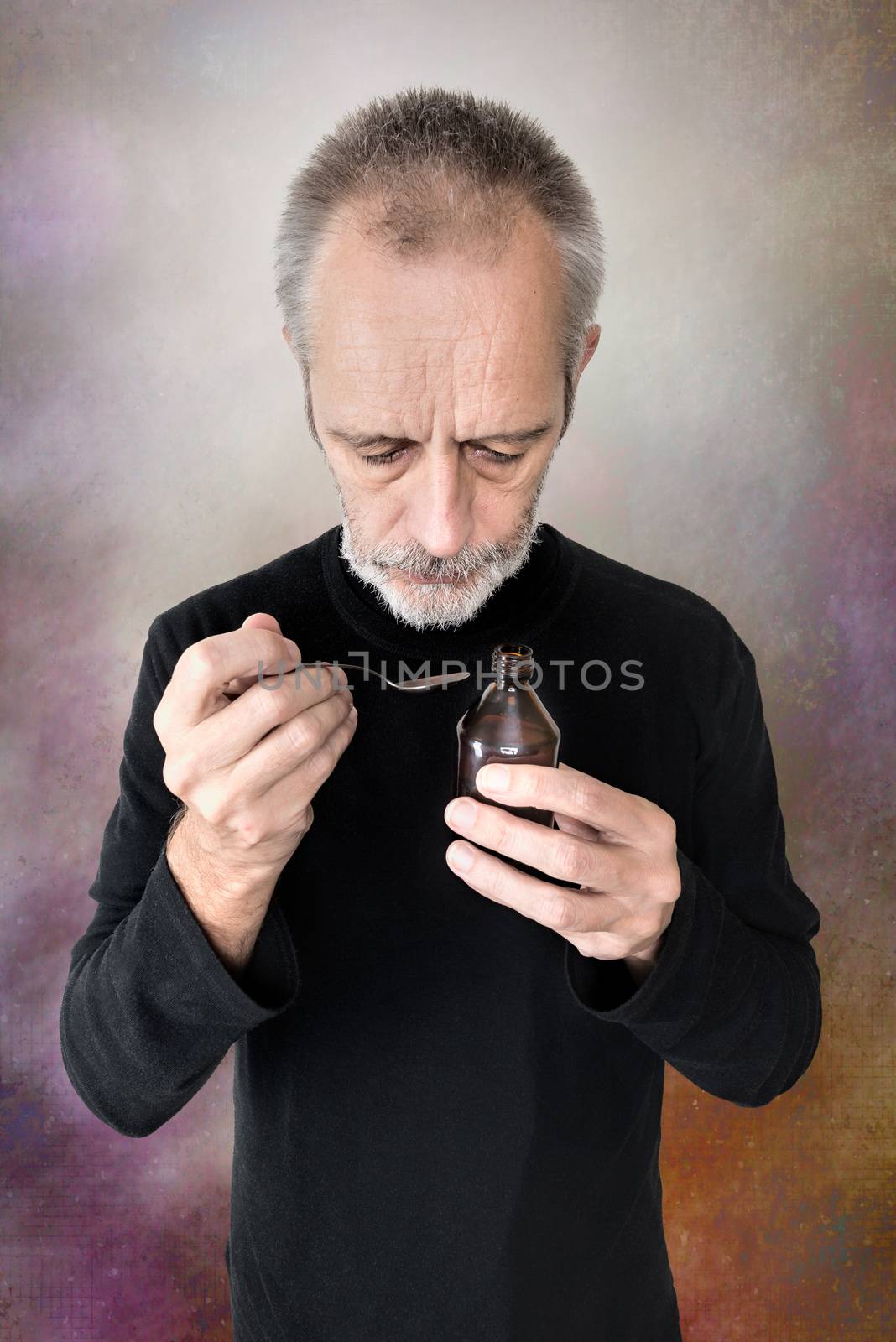 A mature man is pouring cough syrup in a spoon to cure his sore throat and bronchitis