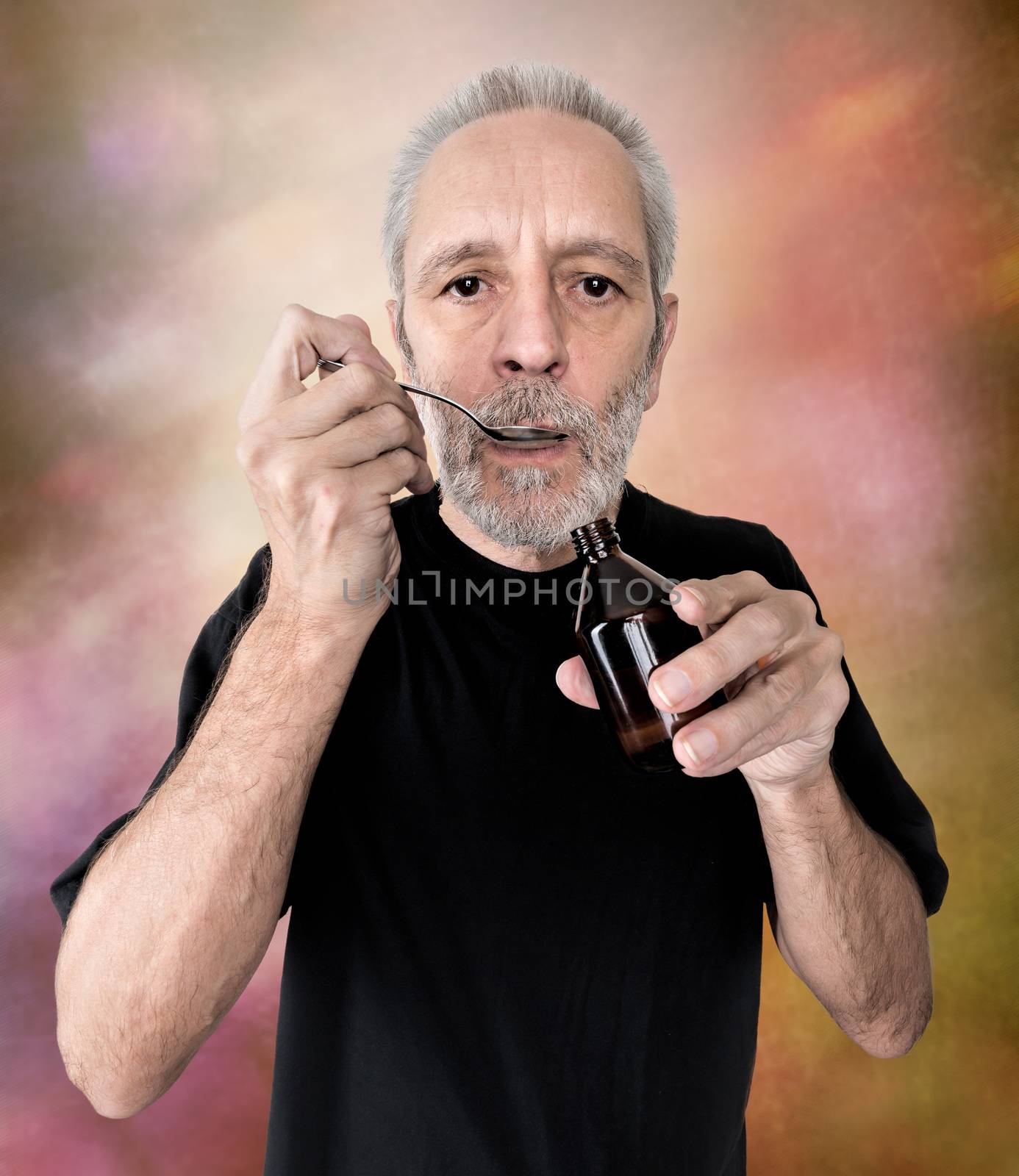 A mature man is drinking a spoon of  cough syrup to cure his sore throat and bronchitis