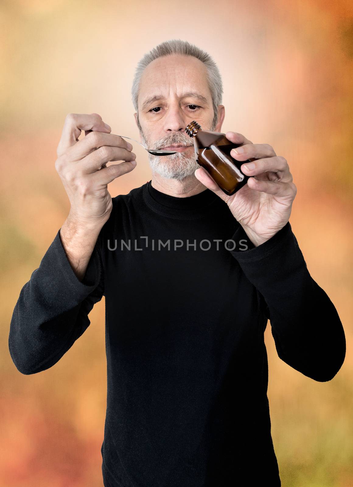 A mature man is pouring cough syrup in a spoon to cure his sore throat and bronchitis