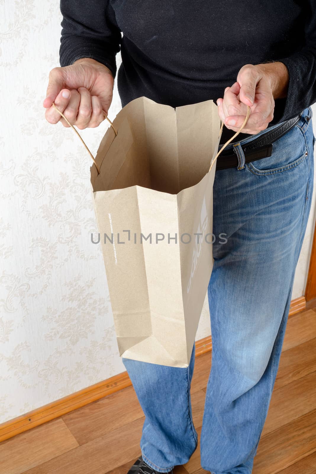 A man in blue jeans and black sweatshirt is looking inside a brown paper bag