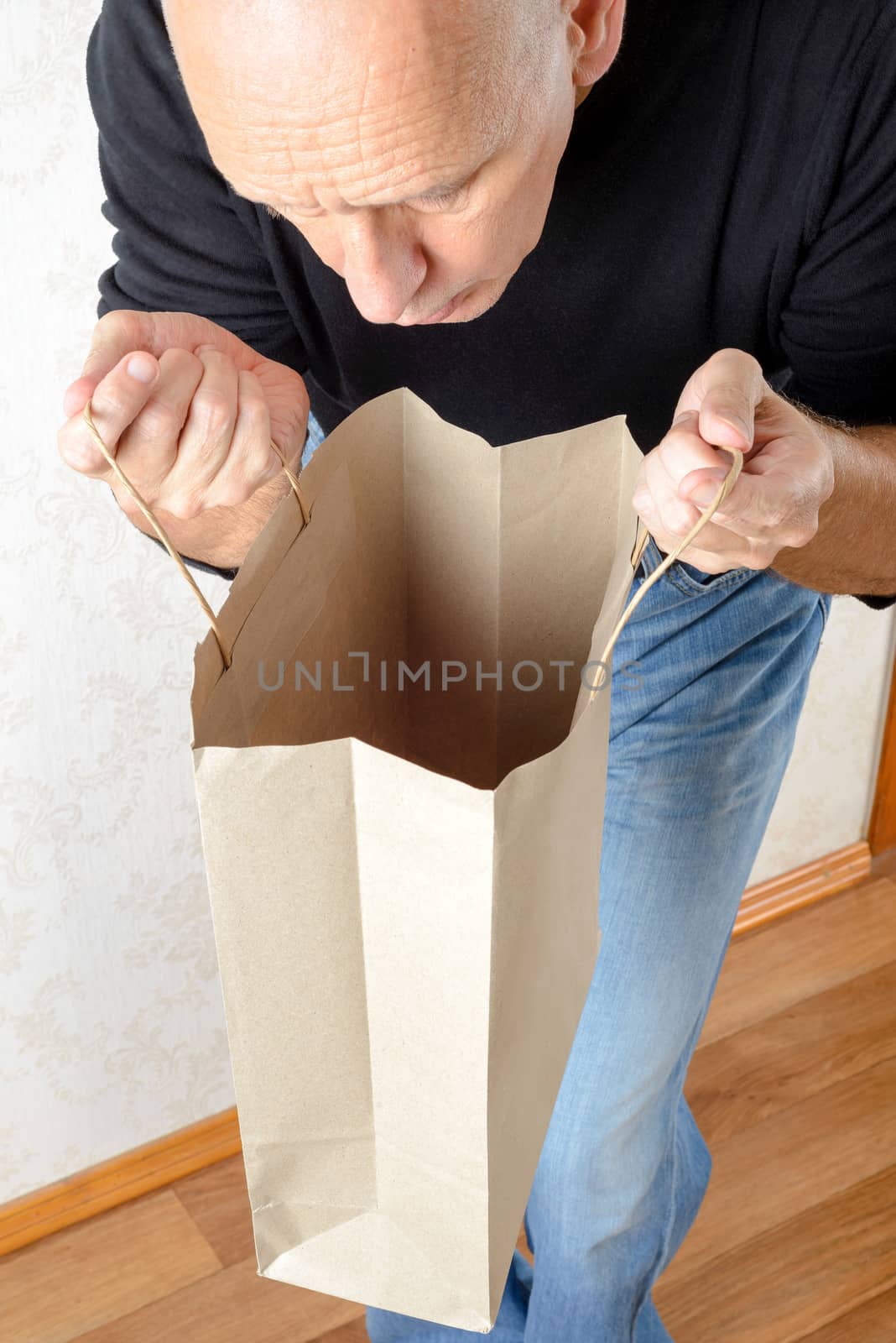 A man in blue jeans and black sweatshirt is looking inside a brown paper bag