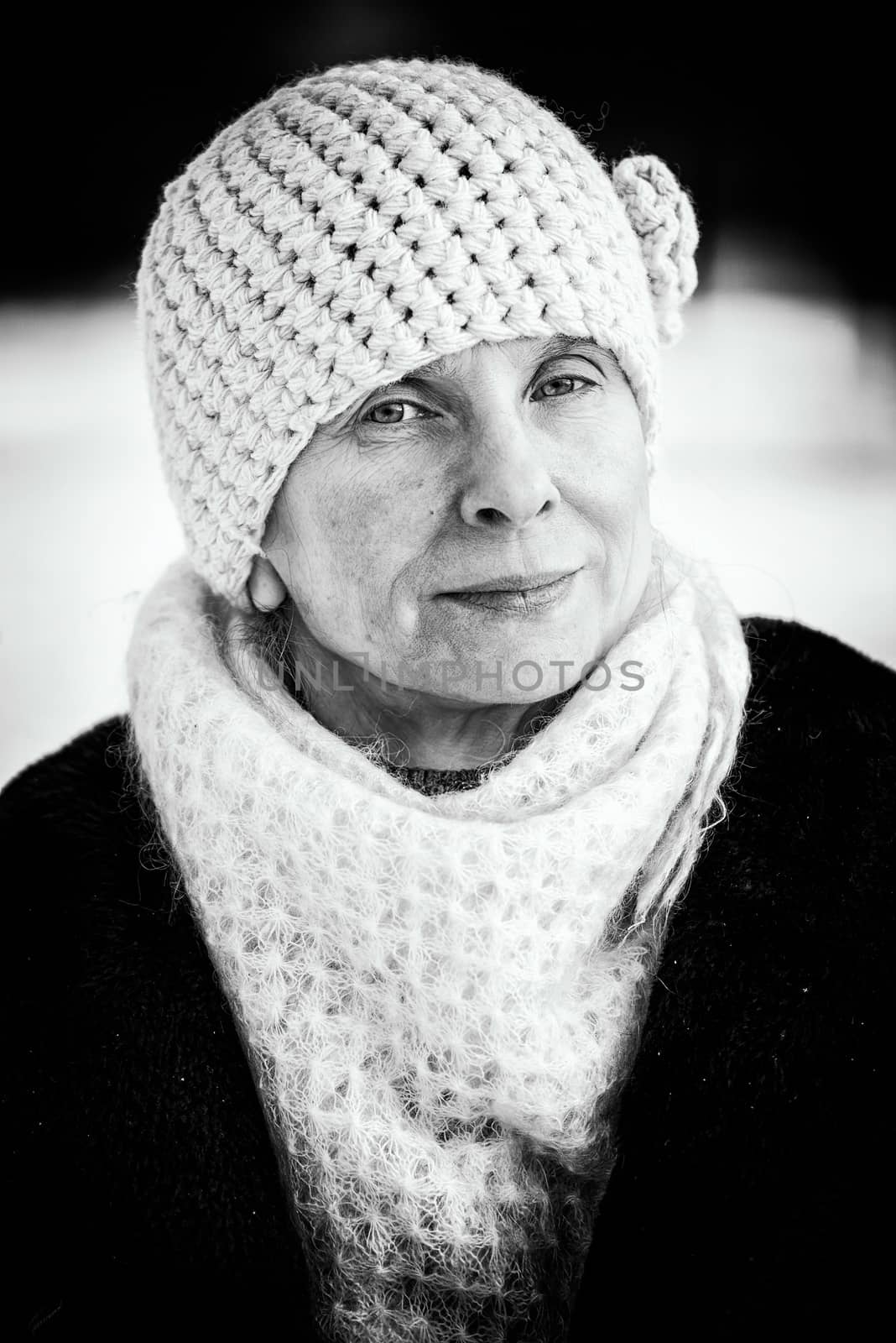 A winter portrait of a senior adult woman wearing a wool cap and a scarf, with a snow background