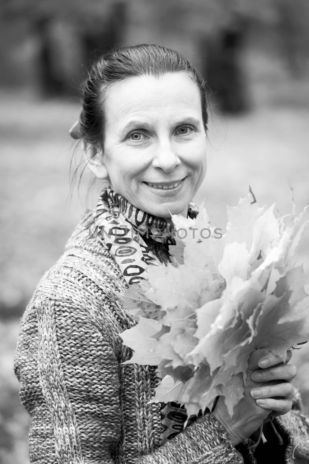 Black and white portrait of a smiling adult caucasian woman is picking yellow maple leaves in autumn in the park
