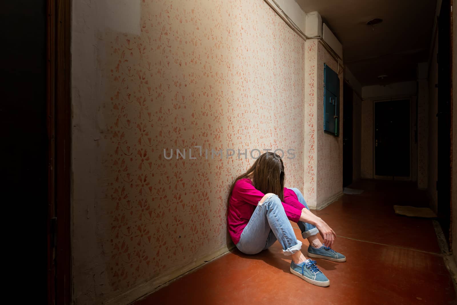 A sad and desperate woman sits in a dark corridor illuminated by a gloomy light. Her pain and her many problems pushed her into complete isolation. His sadness is only equalled by his loneliness.