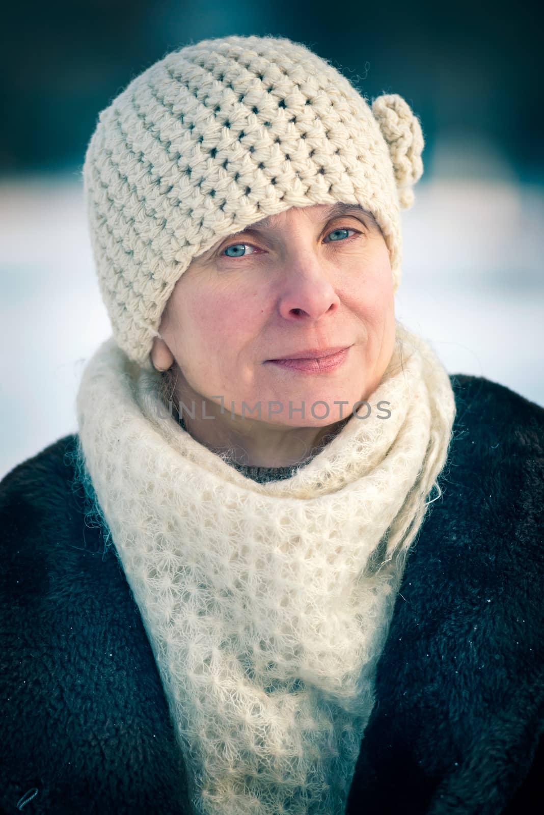 A winter portrait of a senior adult woman wearing a wool cap and a scarf, with a snow background