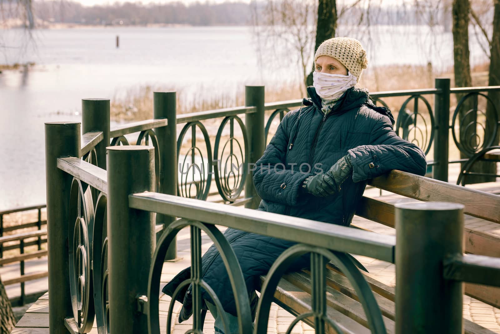 A poor elderly woman wears a homemade mask to protect herself from viruses such as coronavirus, also known as covid-19, or SARS and MERS. She sits on a bench close to the river