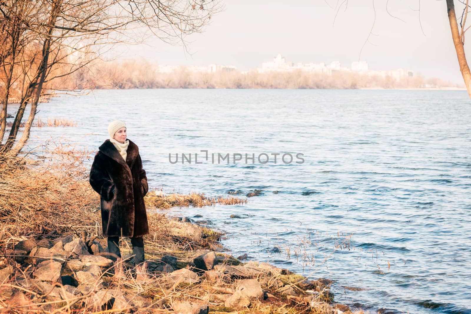A mature woman wearing a warm fur coat and a woolen cap stays close to the Dnieper river in Kiev, Ukraine, during winter