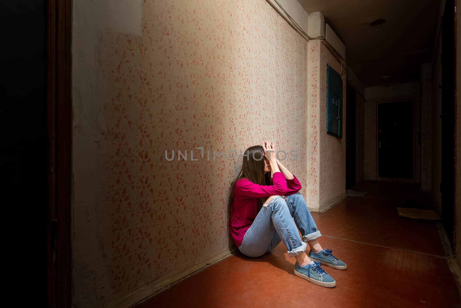 A sad and desperate woman sits in a dark corridor illuminated by a gloomy light. Her pain and her many problems pushed her into complete isolation. His sadness is only equalled by his loneliness.