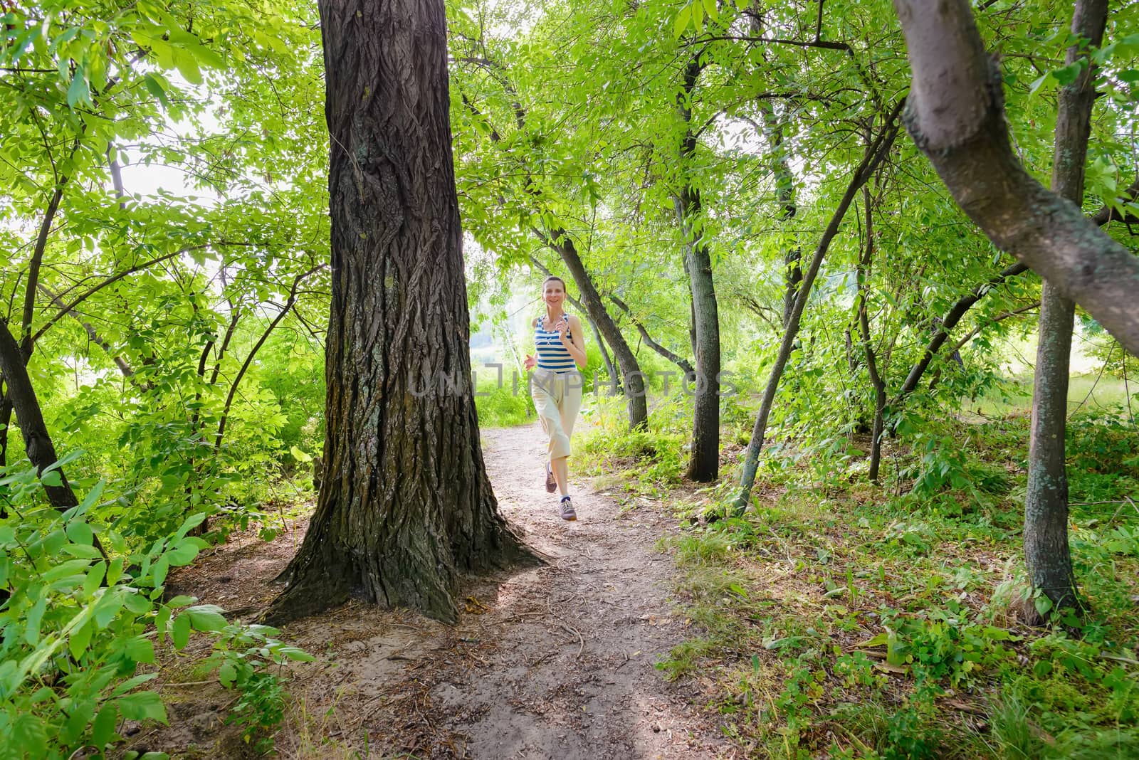 A happy senior woman is running in the forest close to the lake during a warm summer day