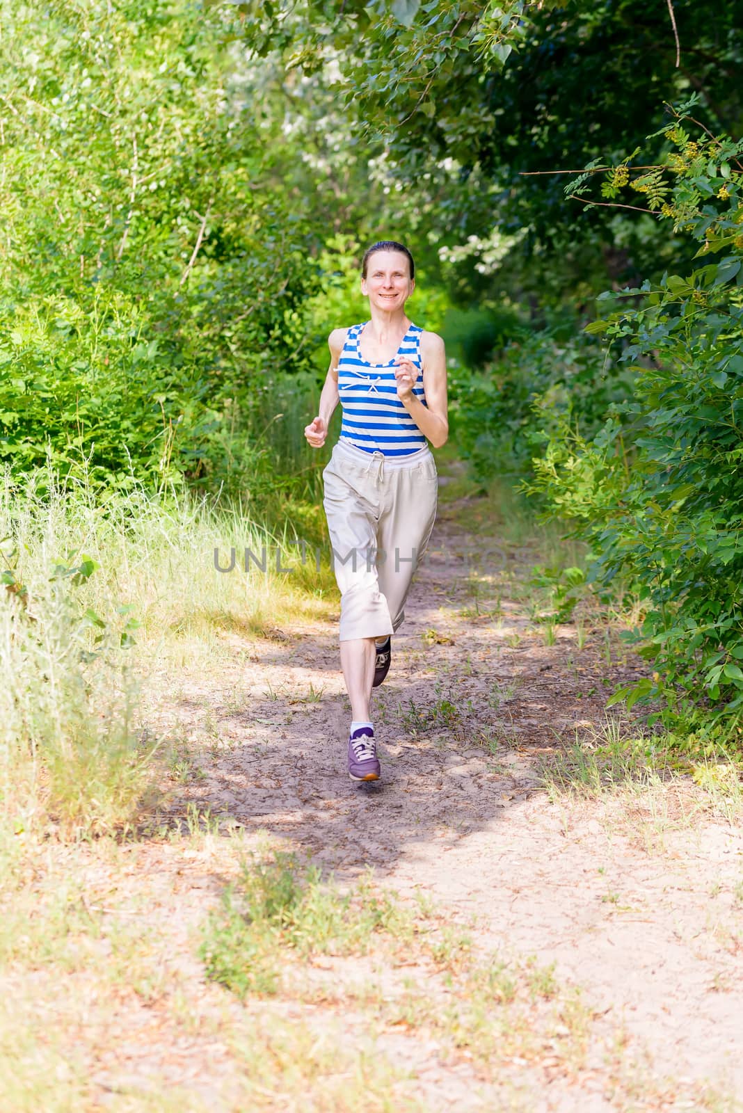 A happy senior woman is running in the forest during a warm summer day