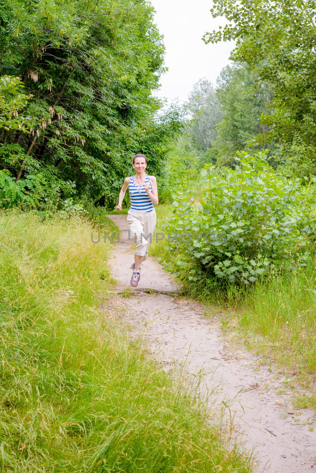 A happy senior woman is running in the forest during a warm summer day