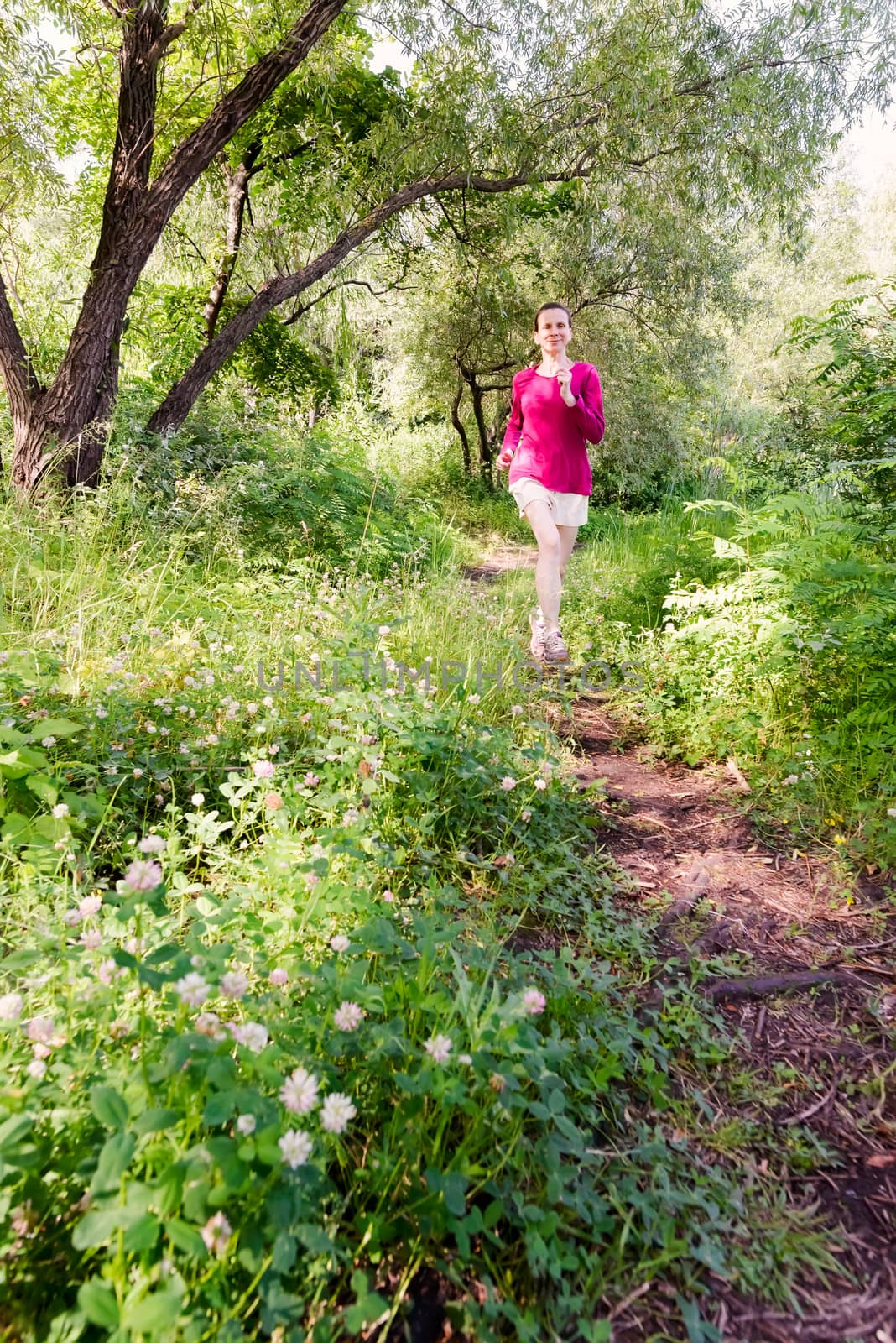 A happy senior woman is running toward the nature in the forest during a warm summer day