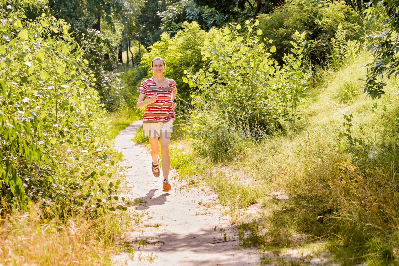 A happy senior woman is running toward the light in the forest during a warm summer day