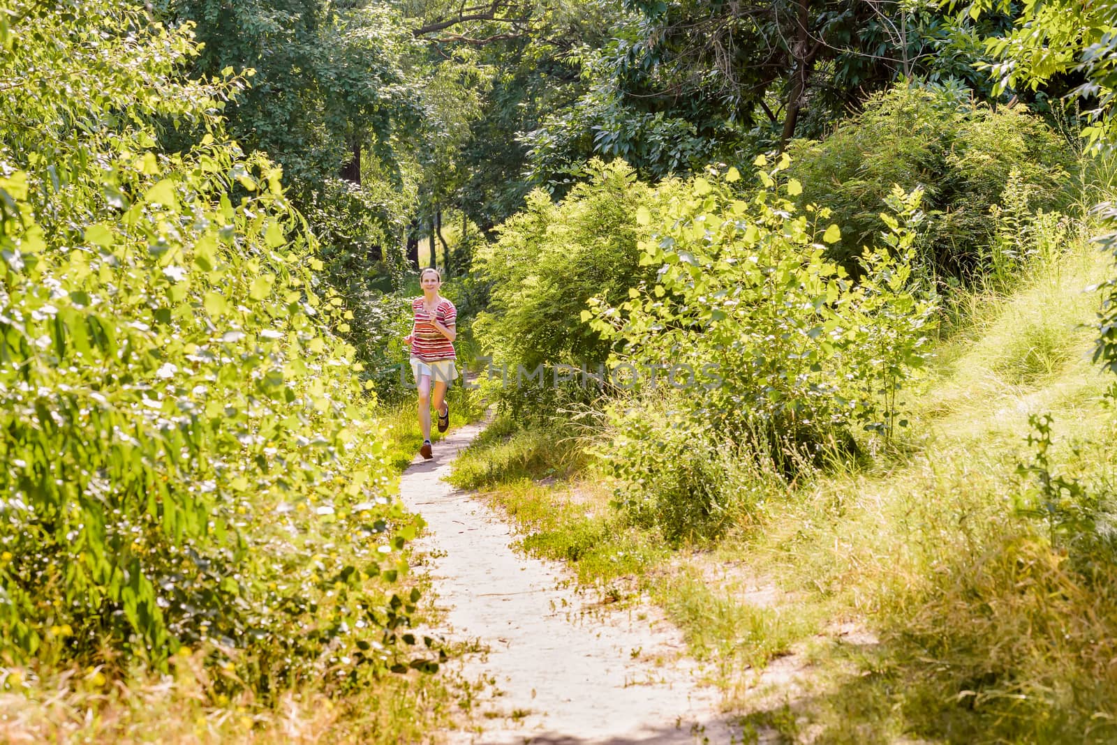 A happy senior woman is running toward the light in the forest during a warm summer day