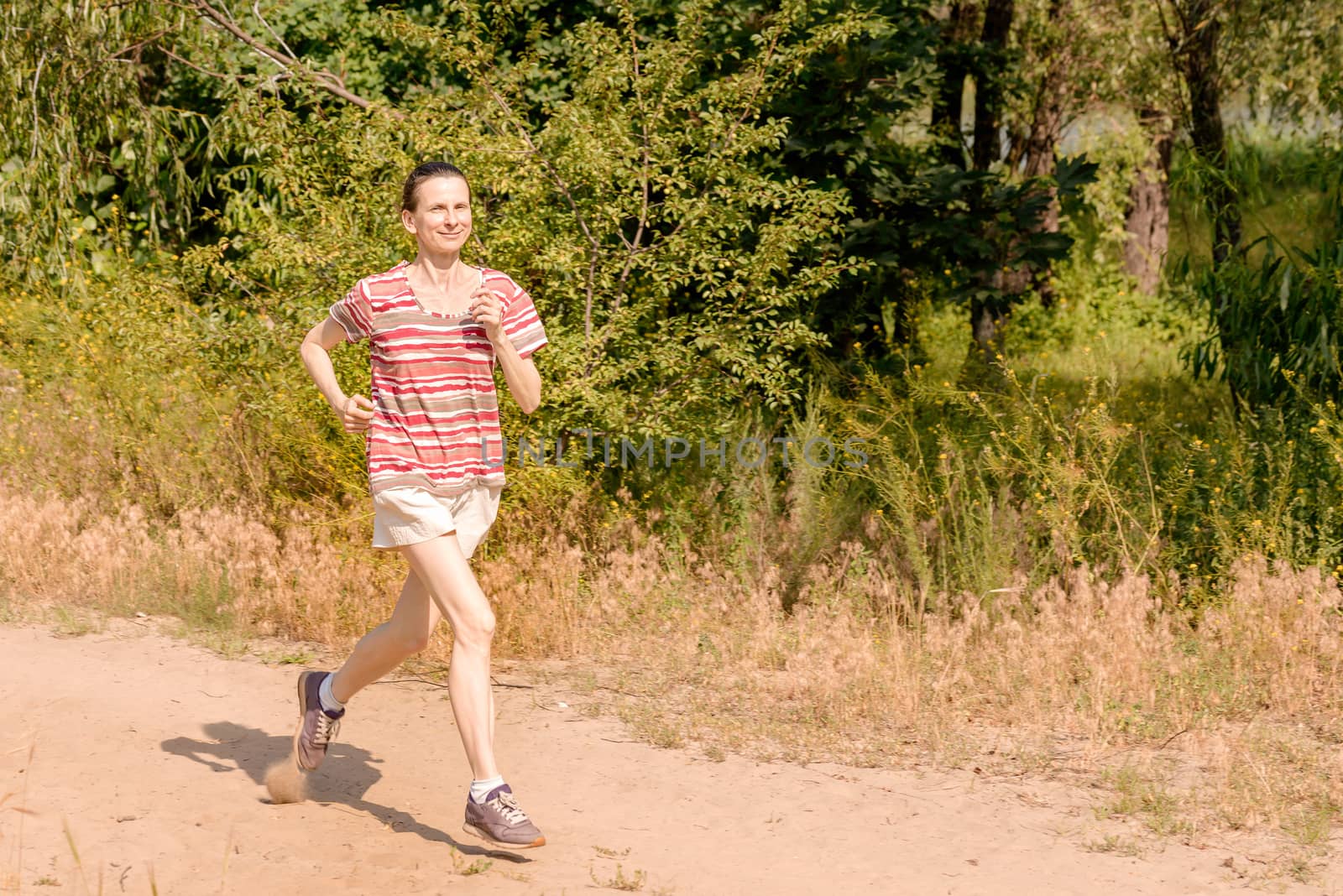 A happy senior woman is running under the sun in the forest during a warm summer day