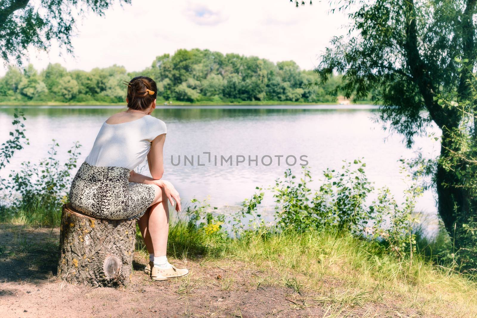 A woman is sitting close to the Dnieper river in Kiev, Ukraine. She is thinking while watching or observing far in the distance, under a warm and soft summer sun