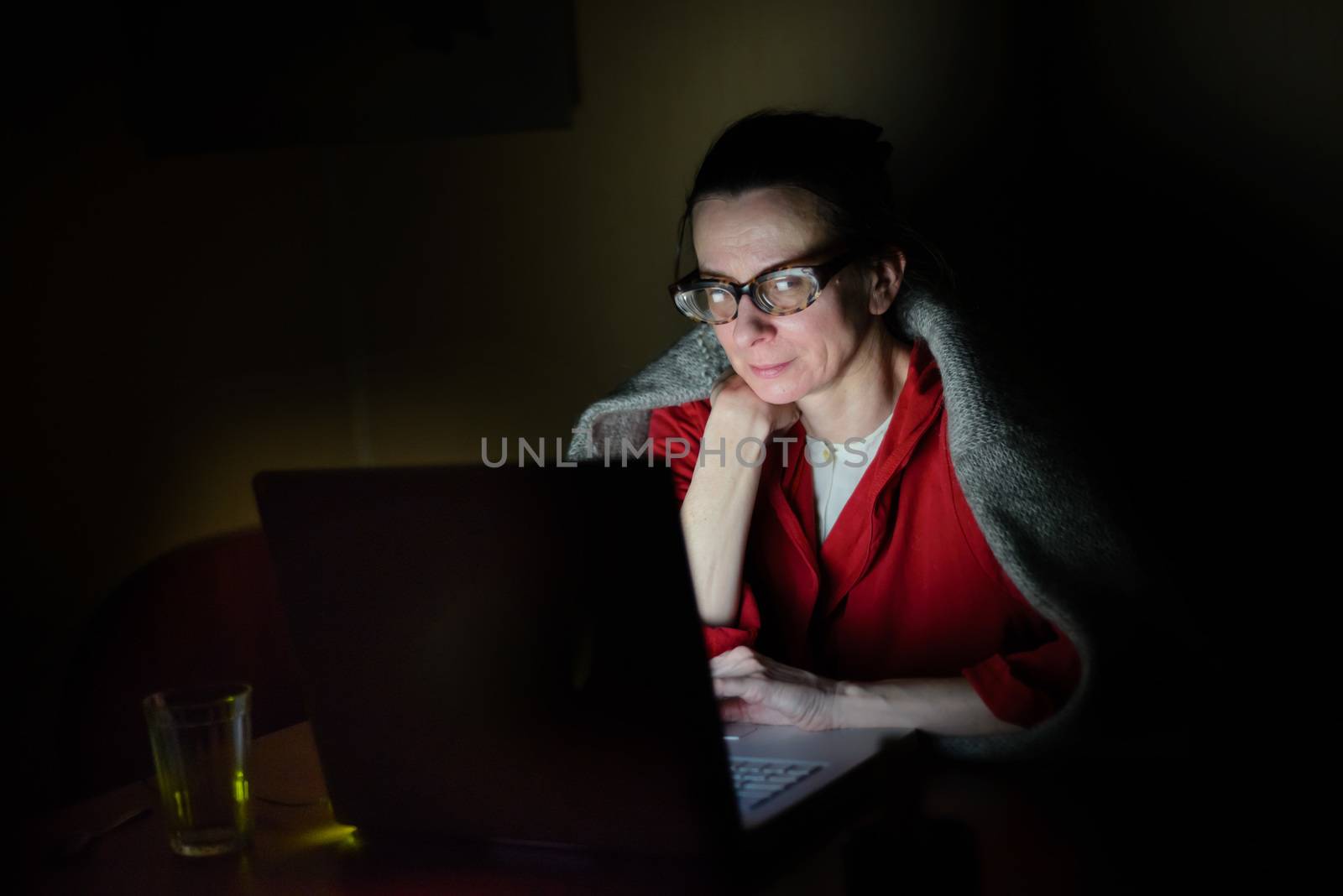 A senior woman using a computer in the dark during a cold winter evening