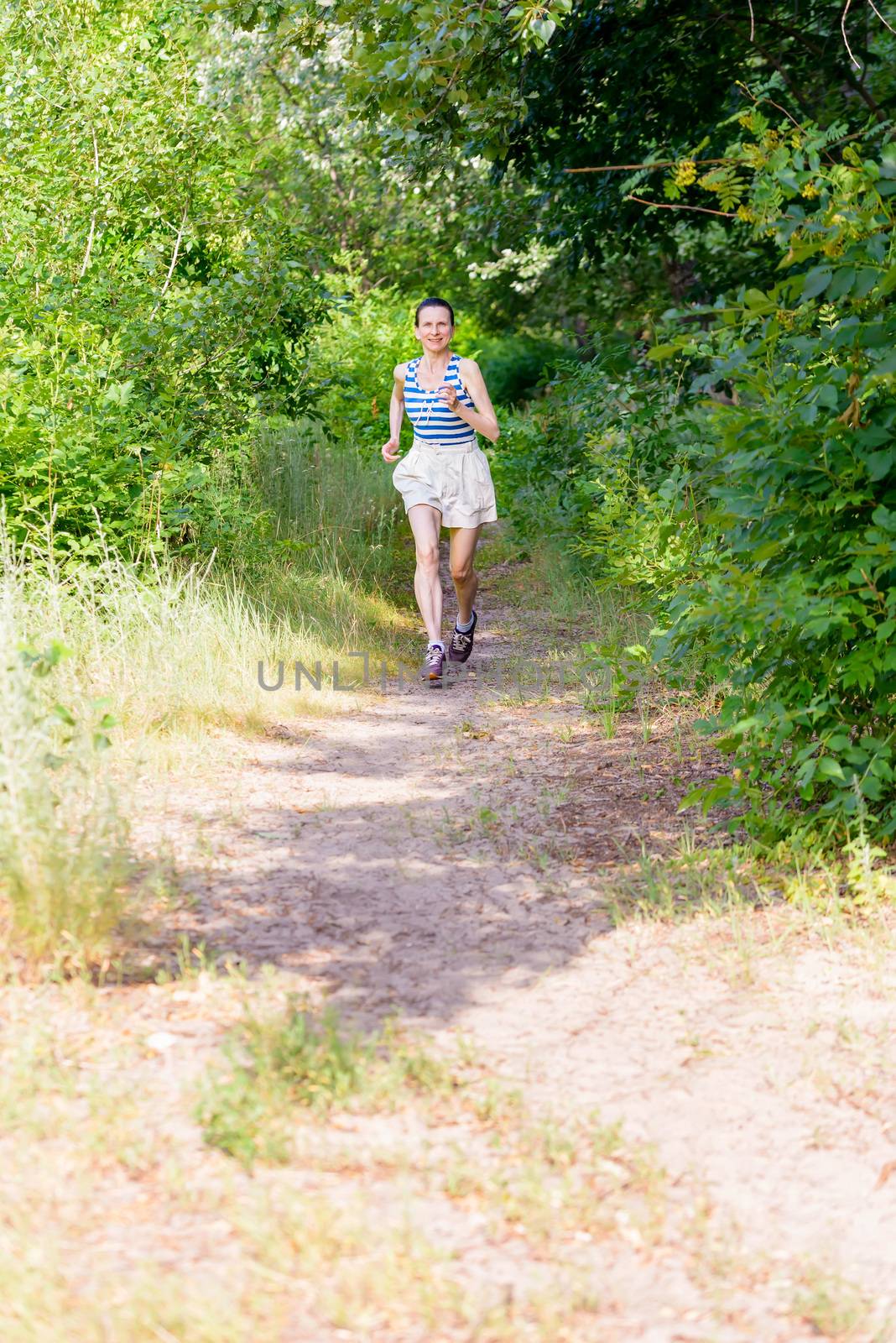 A happy senior woman is running in the forest during a warm summer day