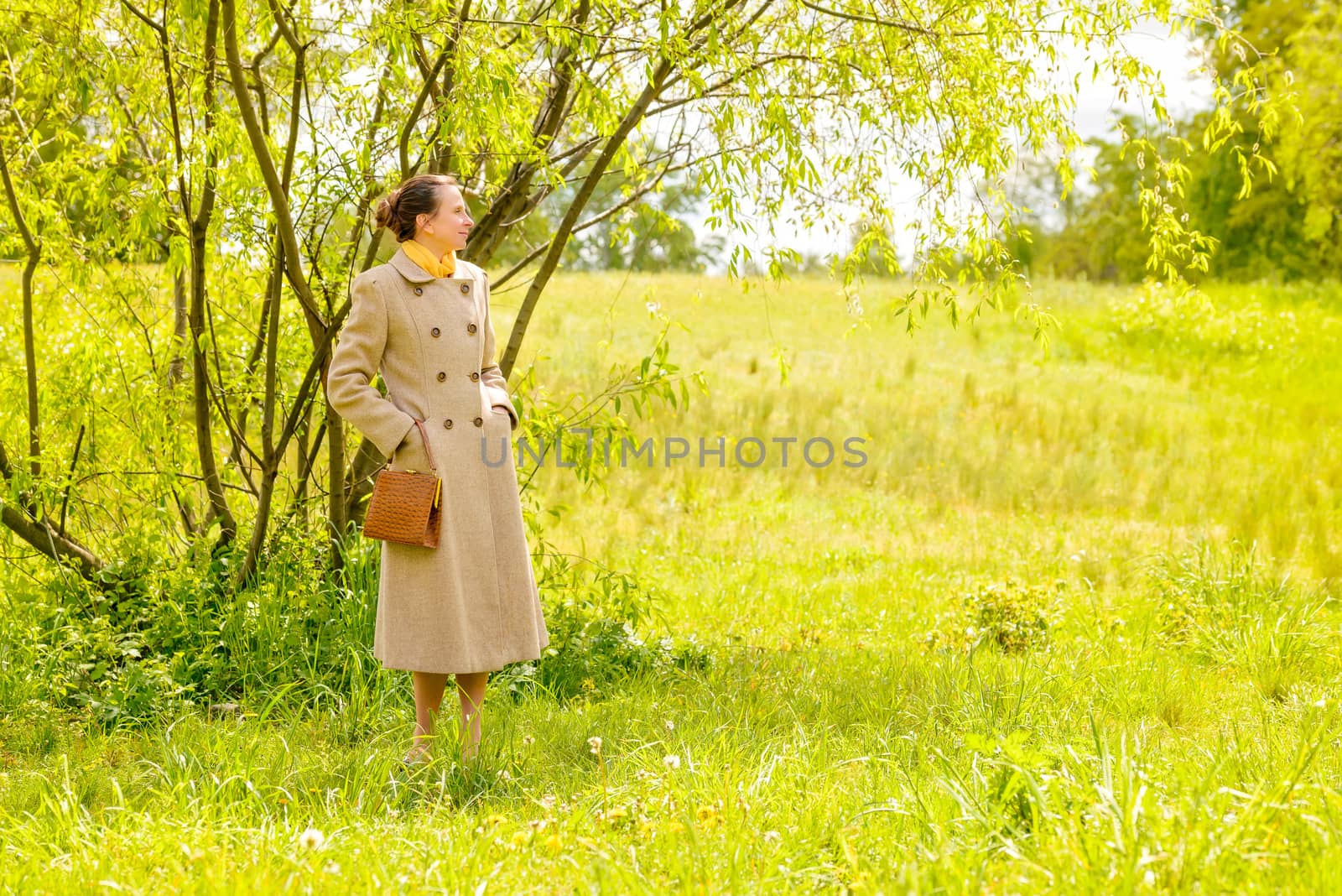 An elegant senior businesswoman, with a coat and a yellow scarf, waiting in the park under the spring sun