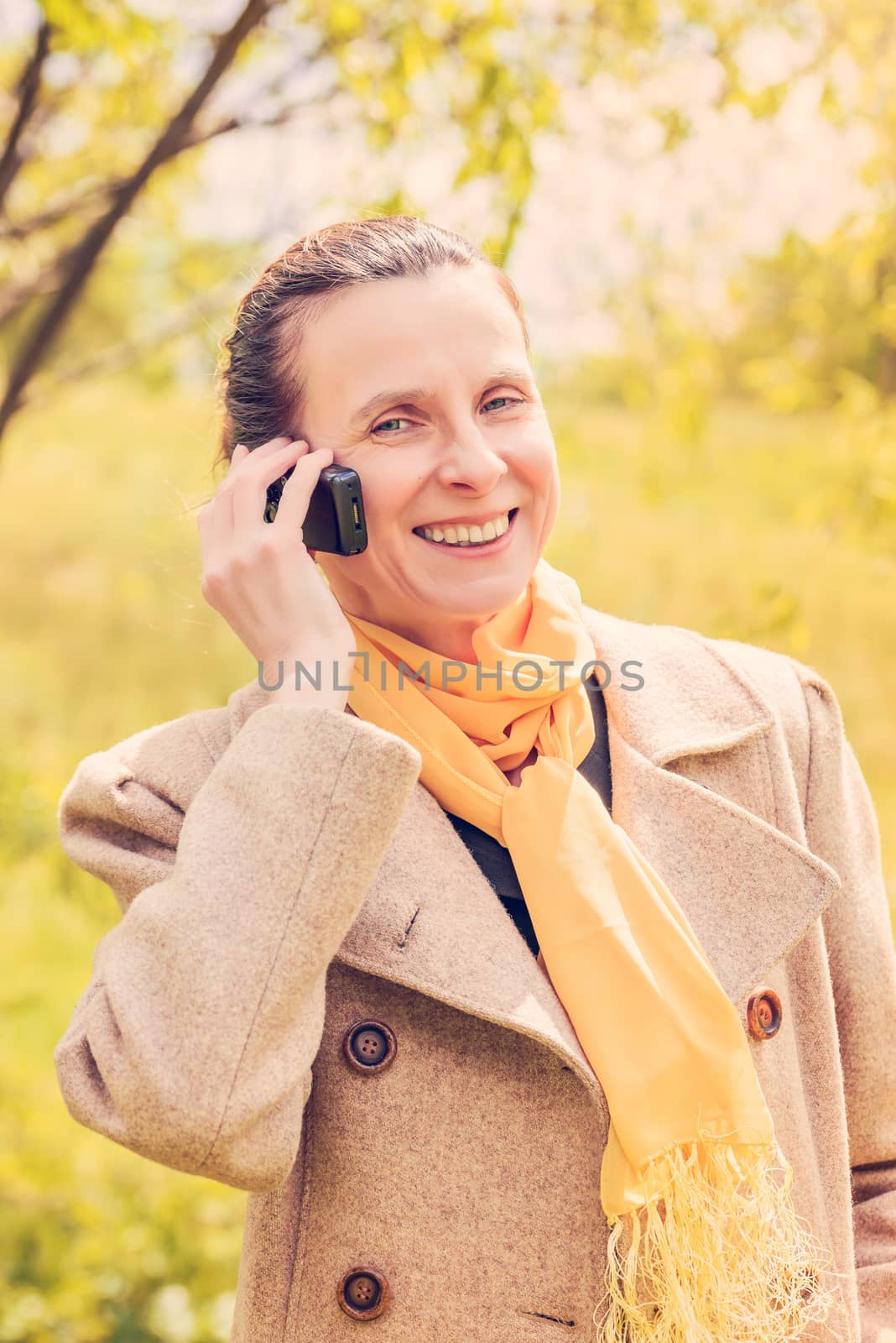 Portrait of a mature and smiling businesswoman wearing a coat and a yellow scarf and calling with her mobile phone