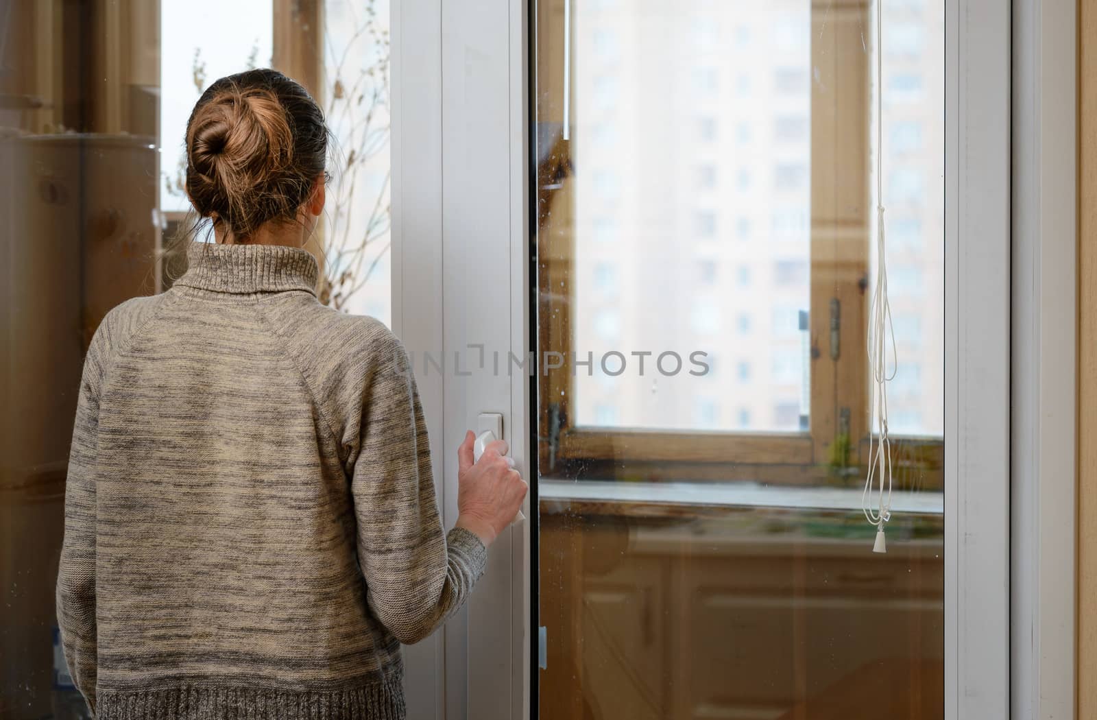 A woman is looking the city through the window during a sad winter day