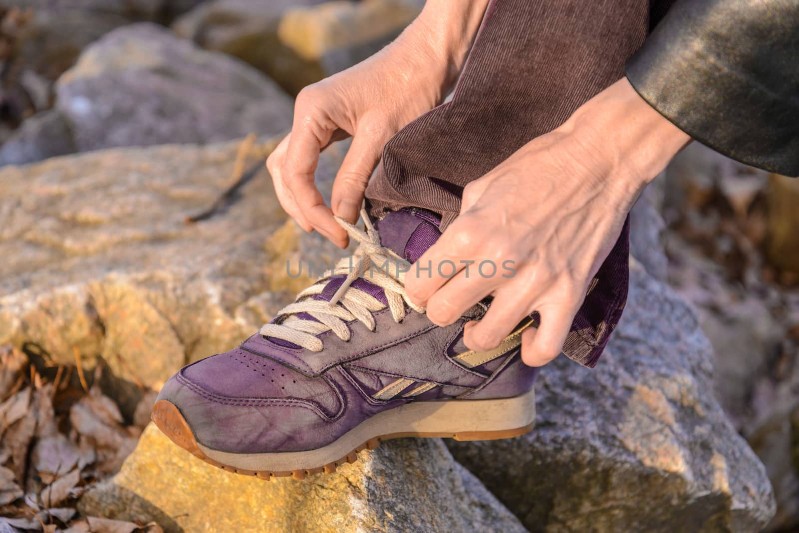 A woman is tying her violet shoes with white laces, during a warm hiking day in mountain