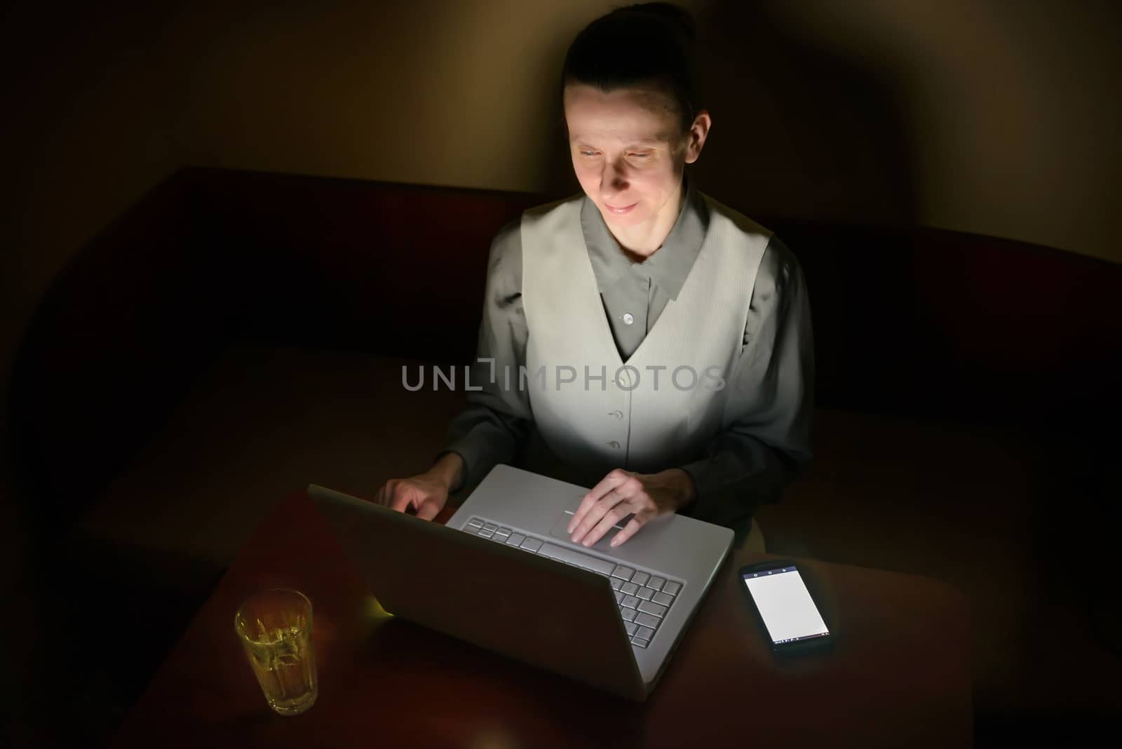 A business woman is using a computer in a dark room. Her face is illuminated by the light from the lcd monitor.