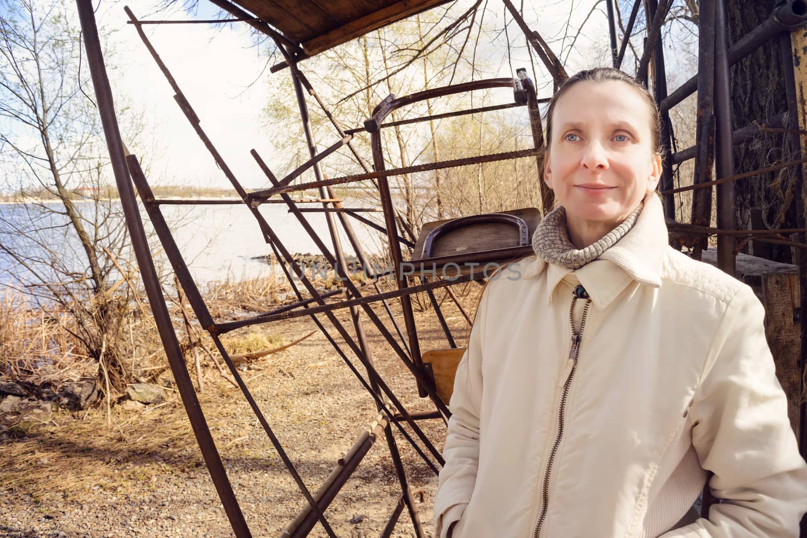 A nice adult woman standing close to the river at the beginning of spring observes something in the distance